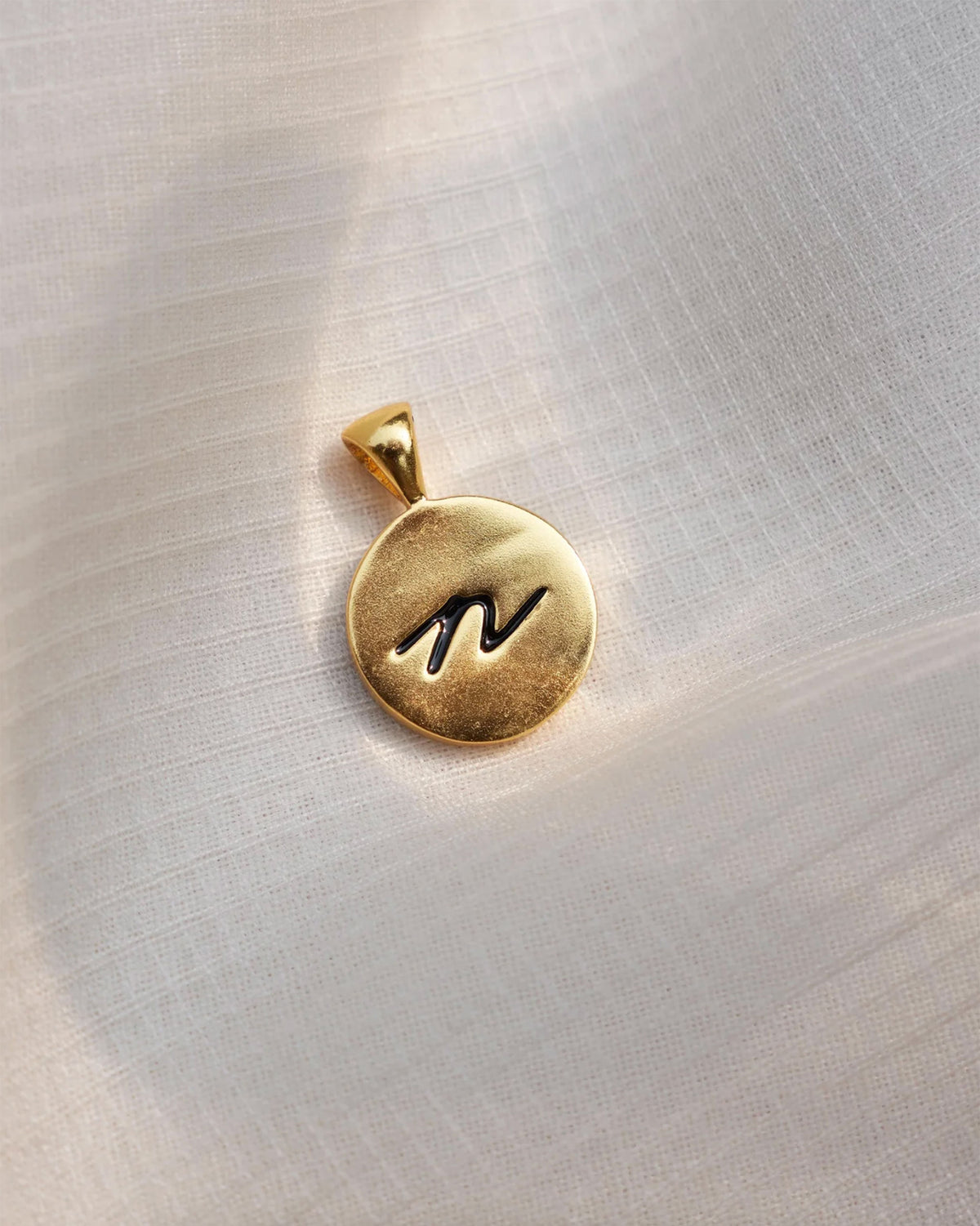 Close-up of a gold Alphabet N charm with a black script n.