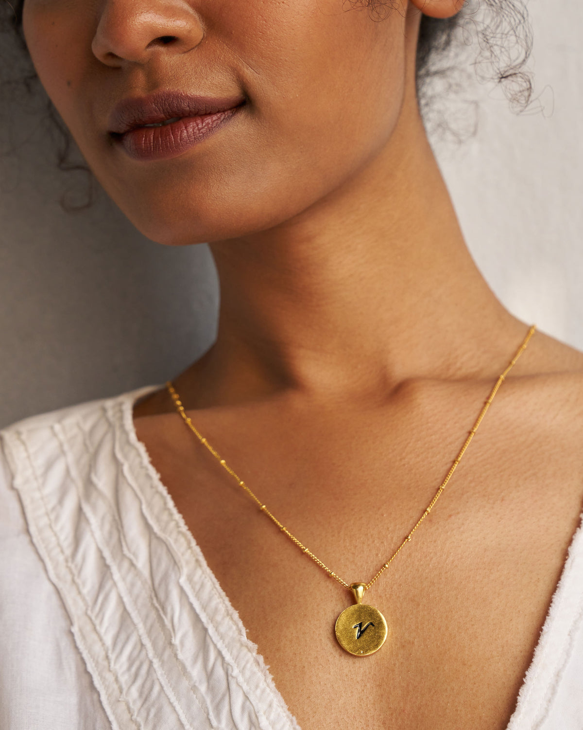 Gold Alphabet V charm with a black script letter v when worn.