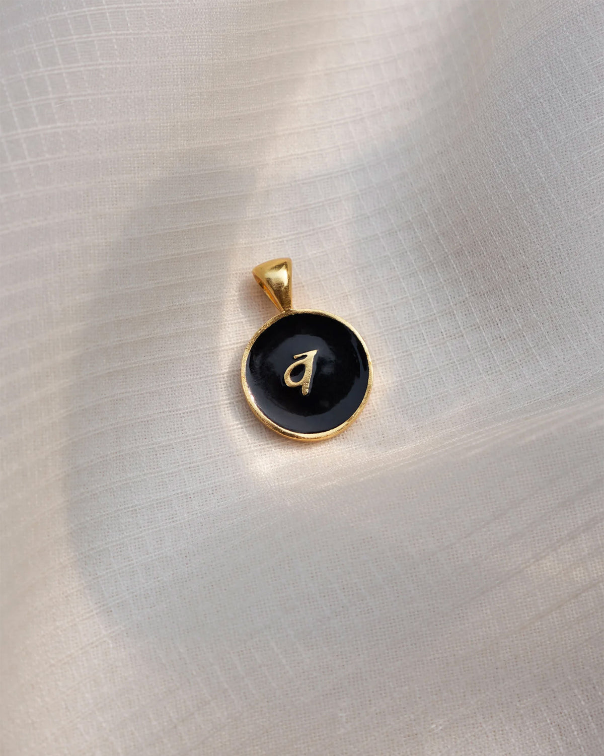 Close-up of a black and gold Alphabet V charm showing a Devanagari letter.