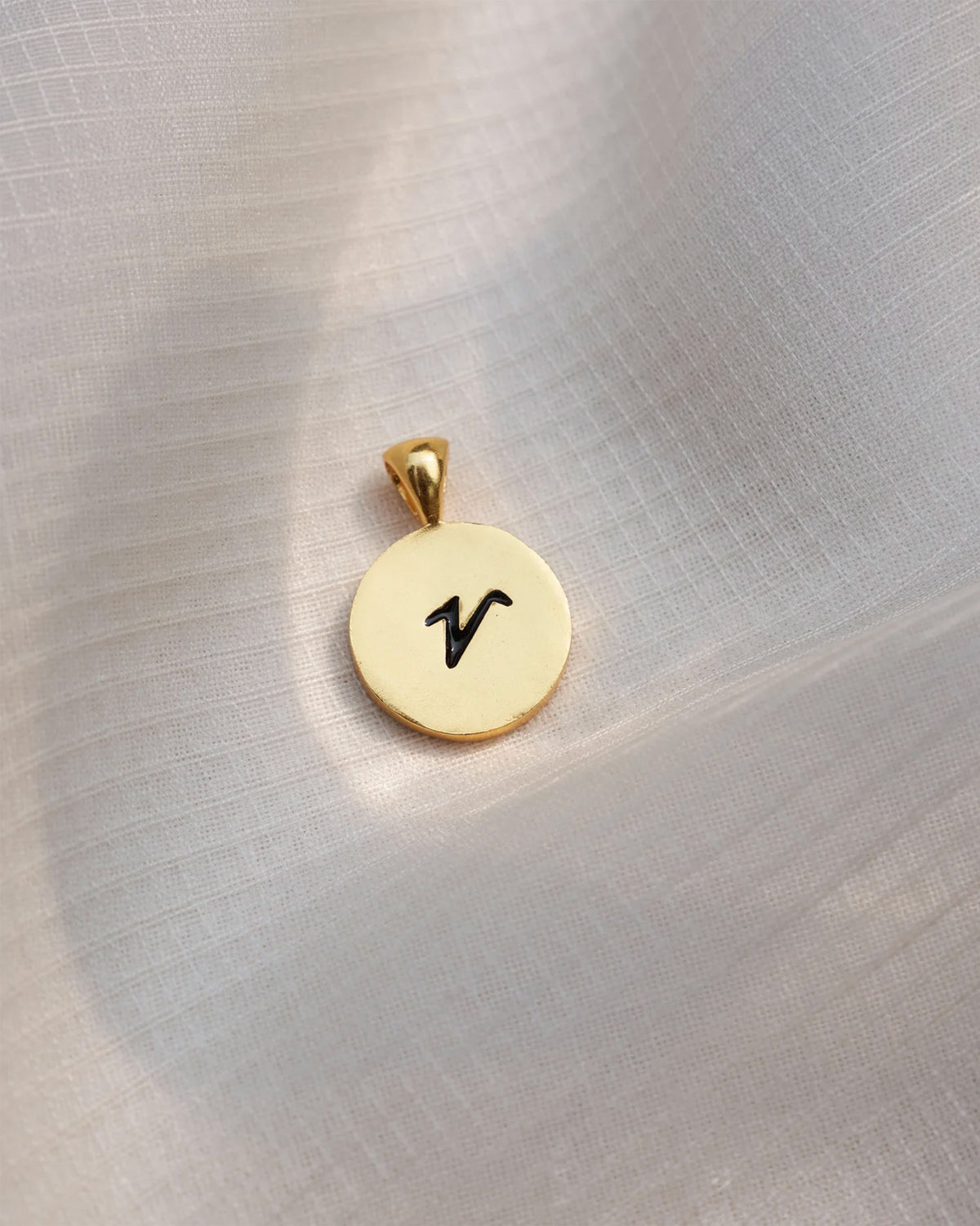 Close-up of a gold Alphabet V charm with a black script v.