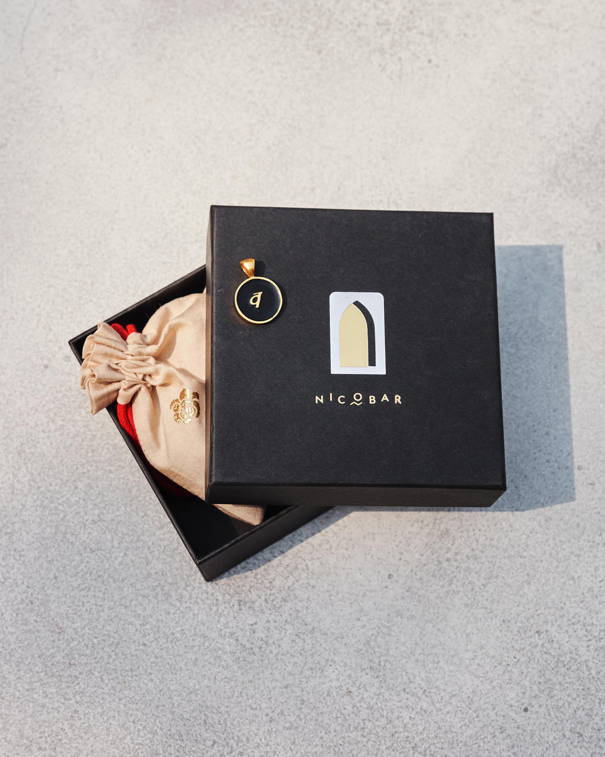 Black and gold Alphabet V charm with व on a Nicobar gift box.