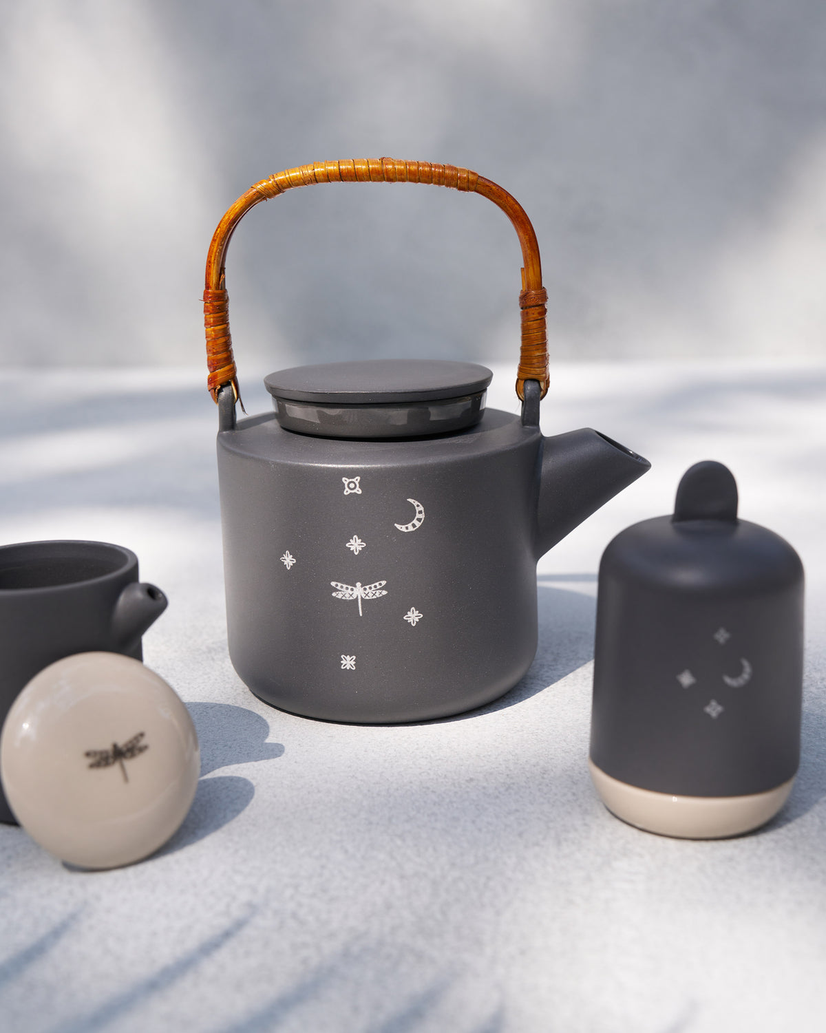 Taramandal teapot with rattan handle beside matching charcoal teaware.