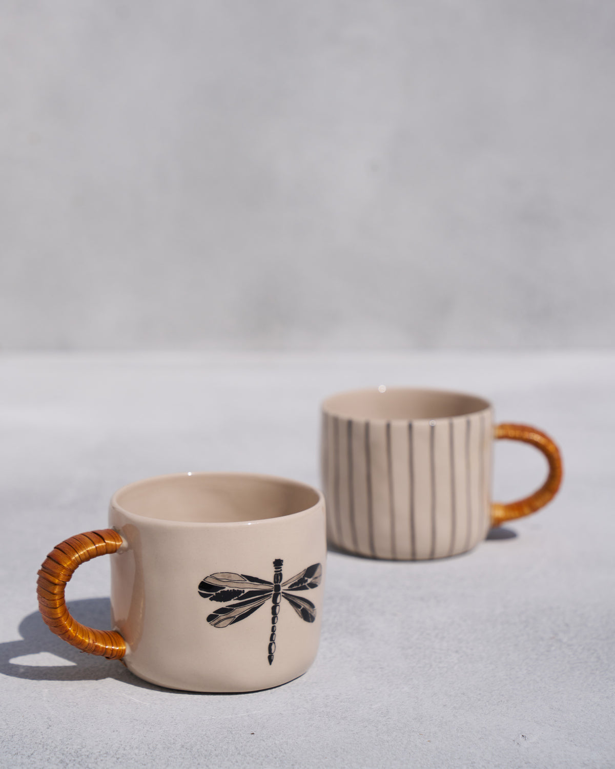 Cream mug with a black dragonfly print and cane handle beside a striped mug.