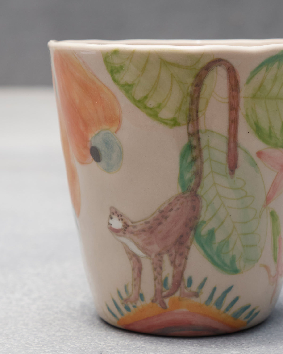Close-up of a macaque and orange cashew fruit painted on a cream ceramic mug.