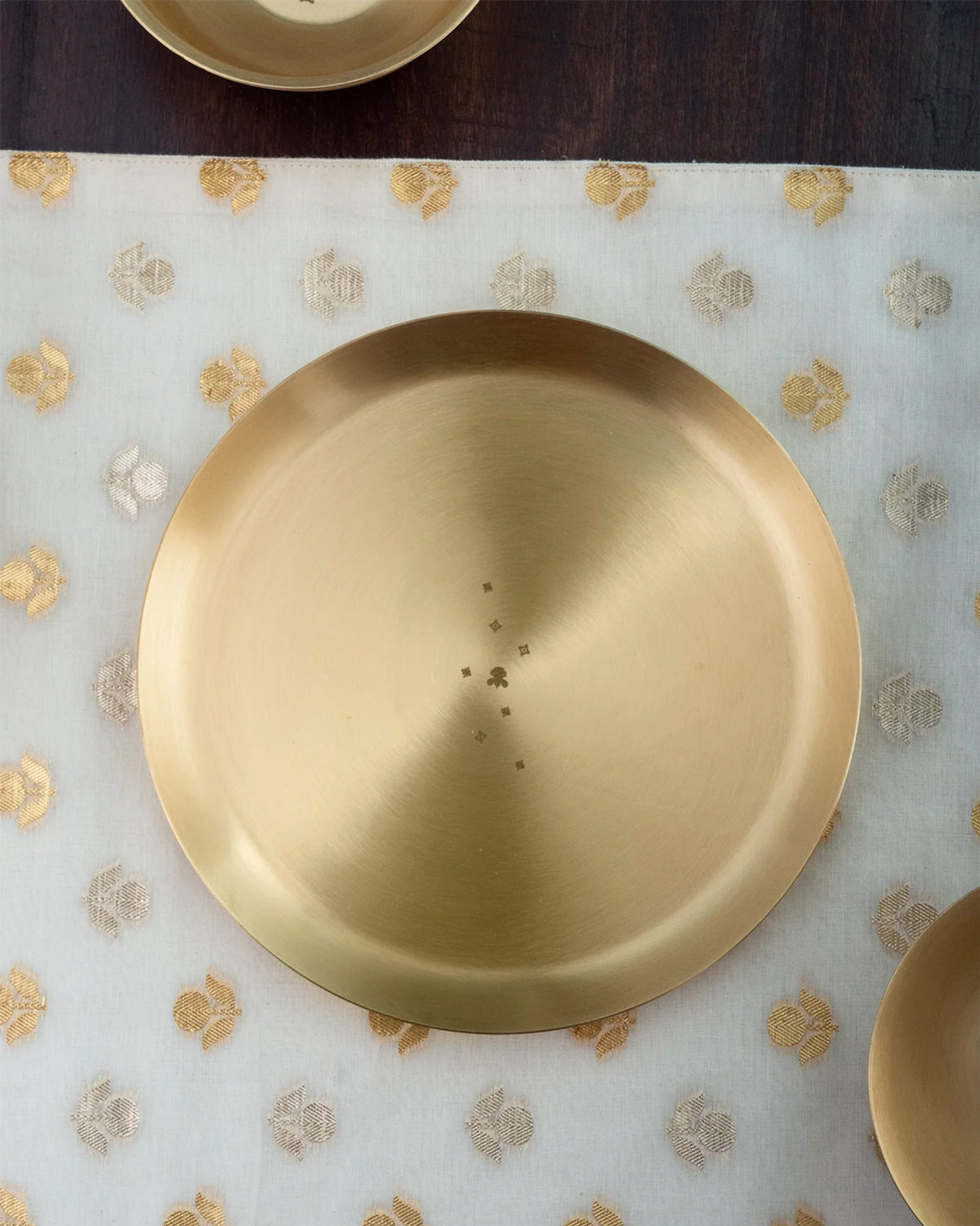 Brass Madhu quarter plate on patterned fabric with matching pieces.