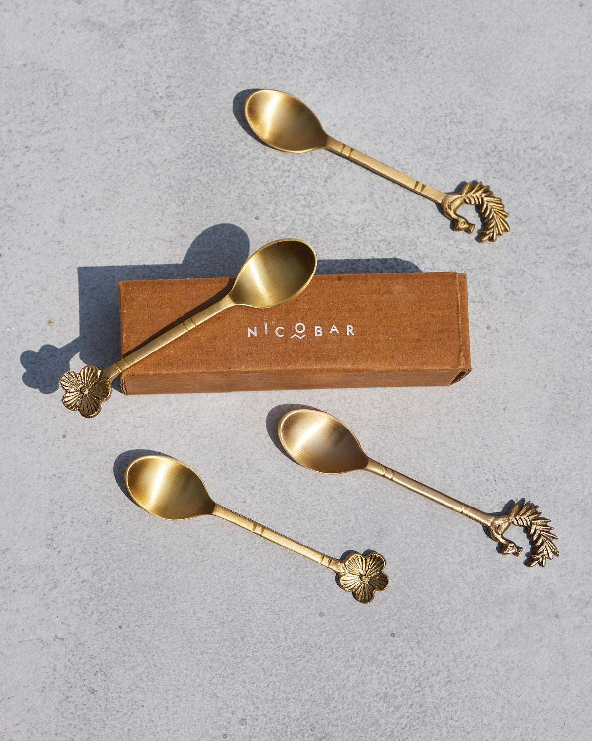 Brass Mizo coffee spoons arranged around a Nicobar gift box.
