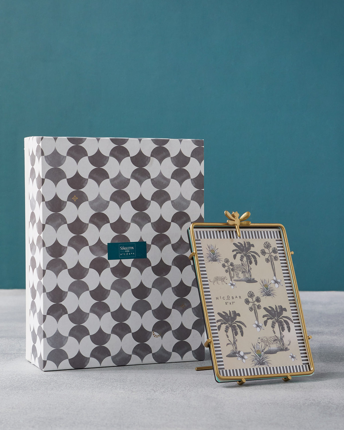 Gold Nizara photo frame with a dragonfly finial beside its patterned gift box.