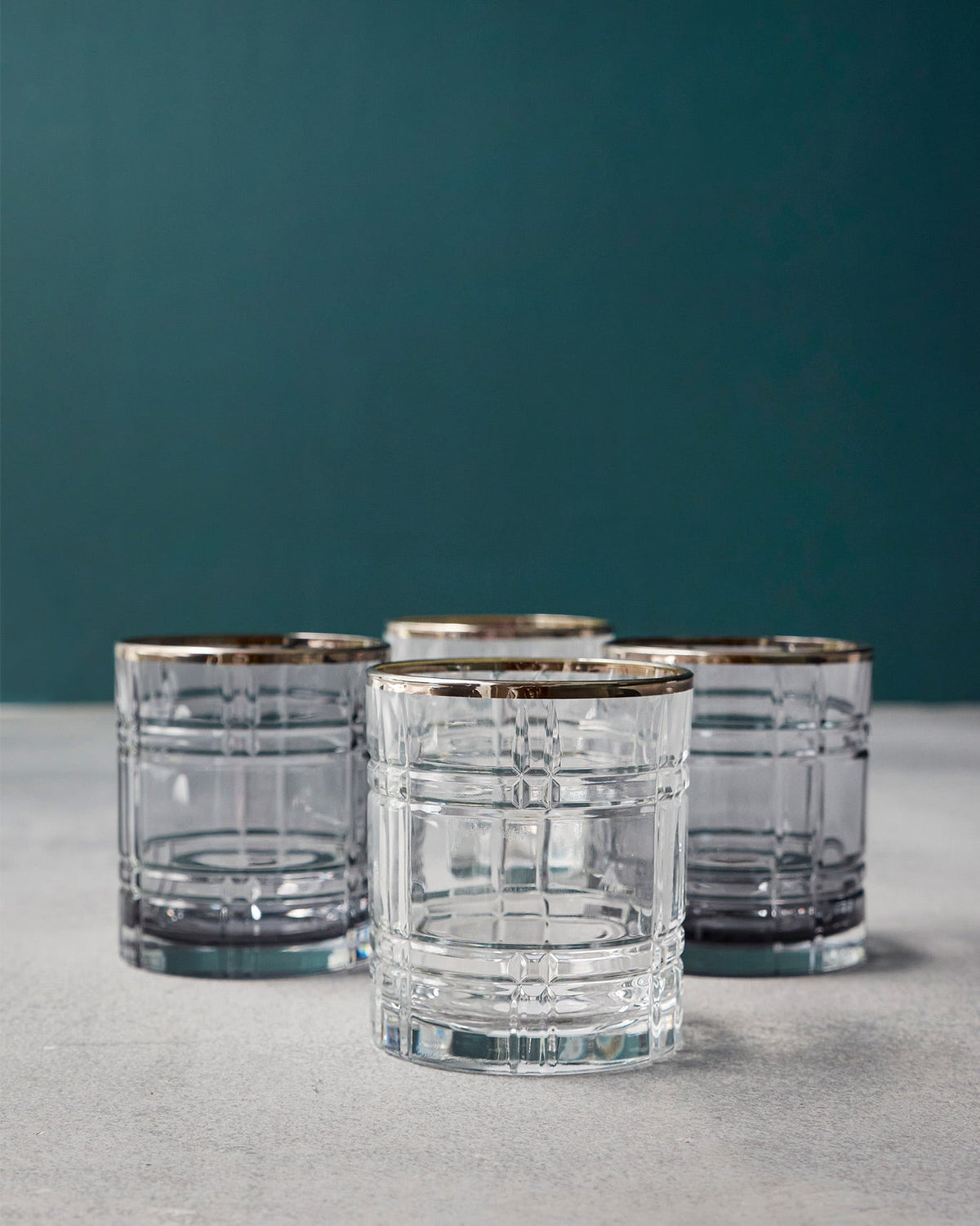 Set of four clear Celeste whiskey glasses with a grid pattern and gold rims.