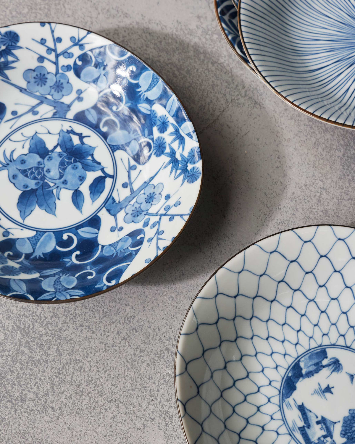 Donburi bowls with blue blossom, lattice, and radial patterns on a grey surface.