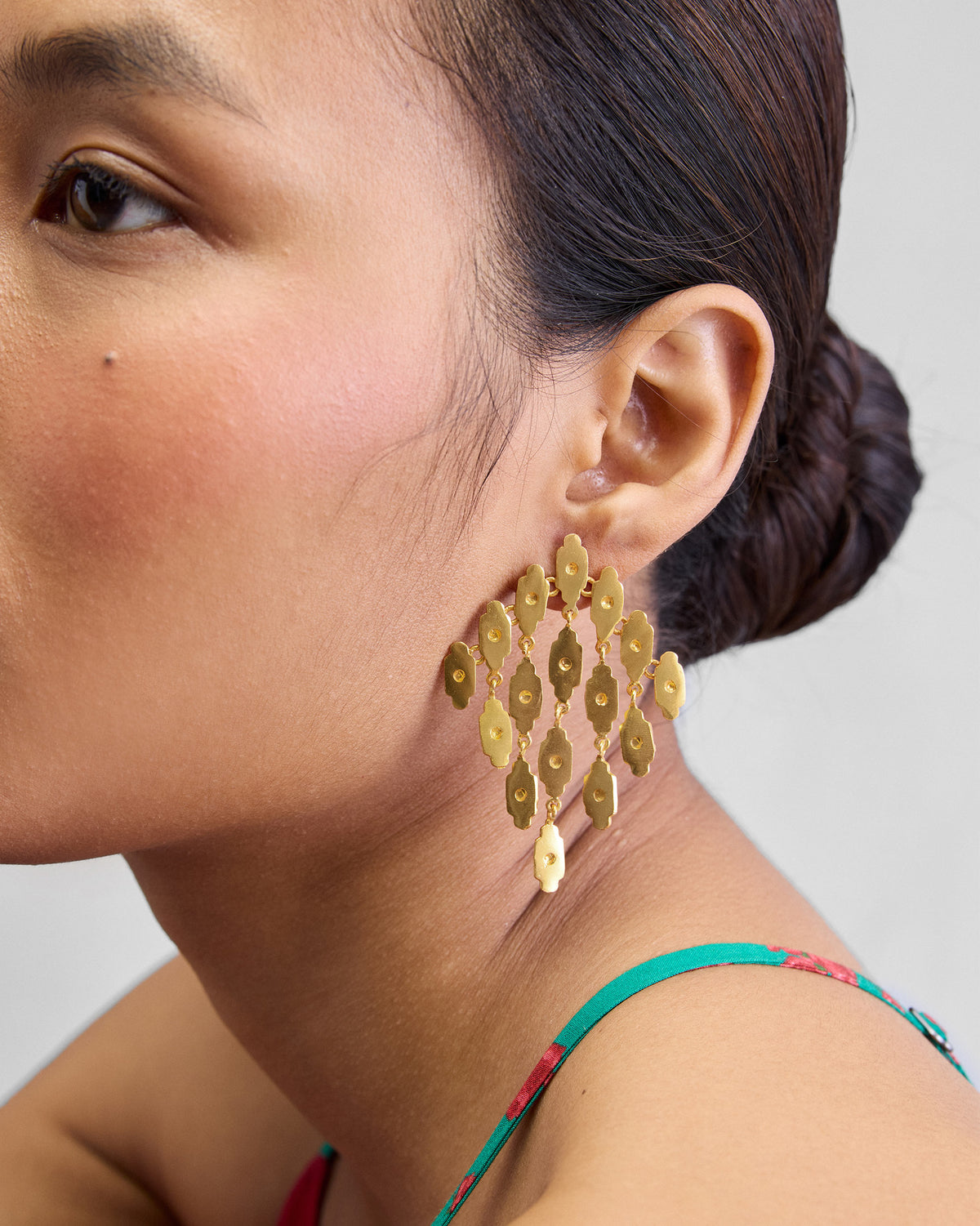 Person wearing gold Zedi Drop Earrings with a cascade of small leaf-shaped plates.