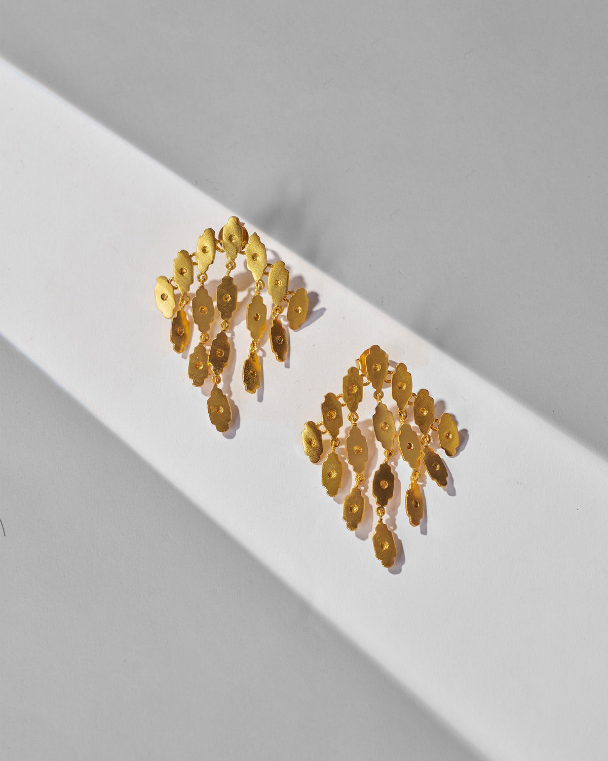 Pair of gold Zedi Drop Earrings laid flat.