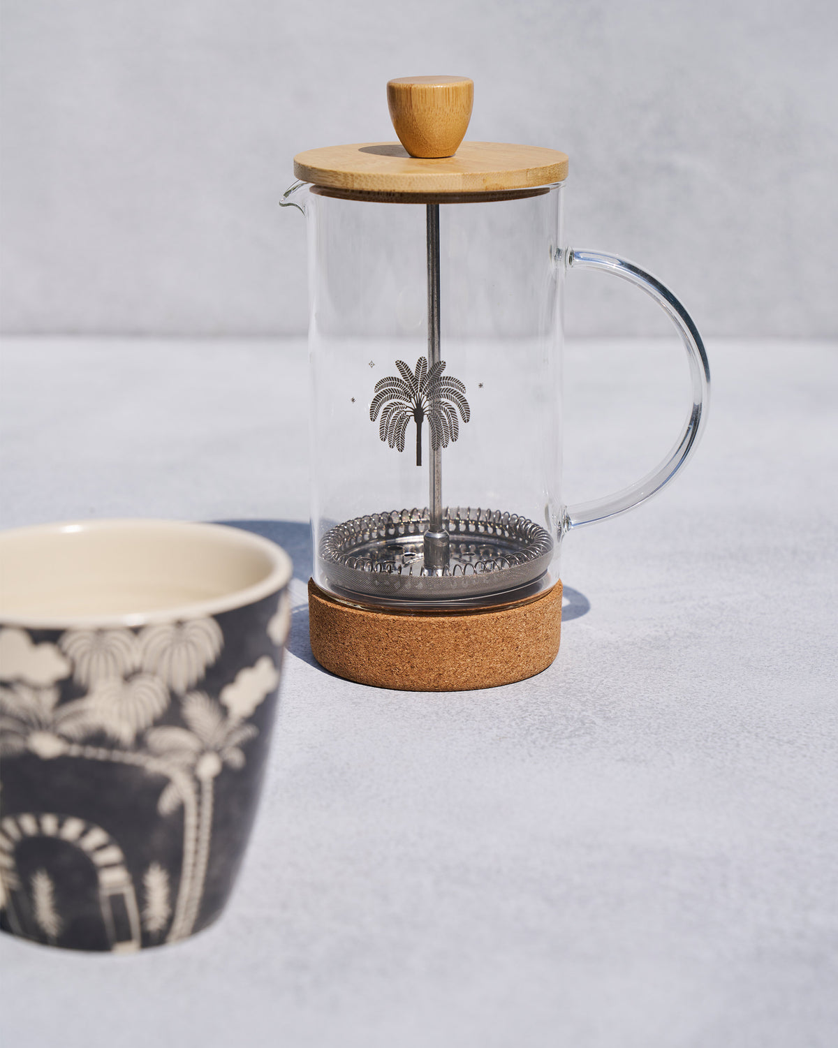 Toddy French press with palm motif and cork base beside a matching mug.