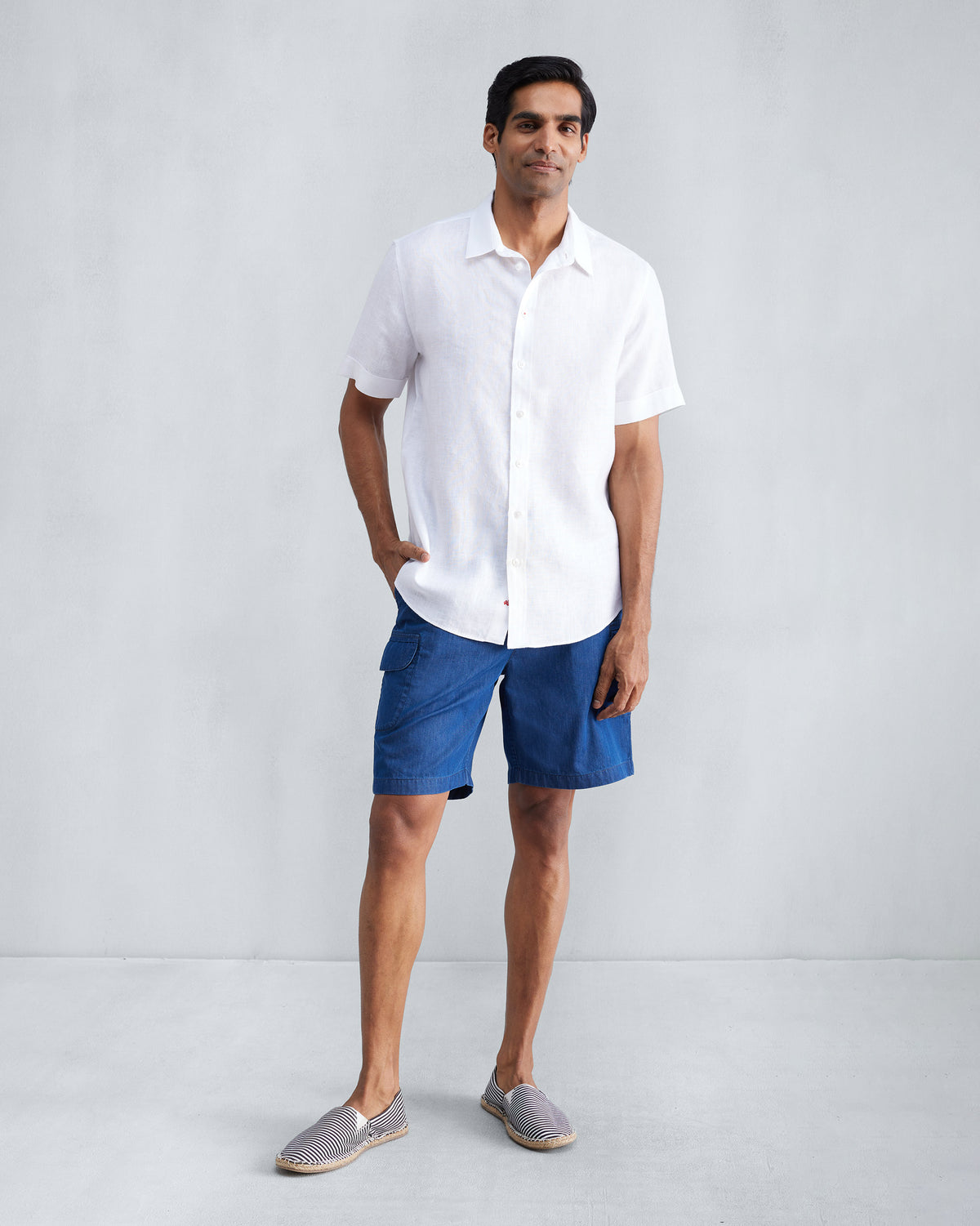 Person wearing a white half-sleeve shirt untucked over blue shorts.