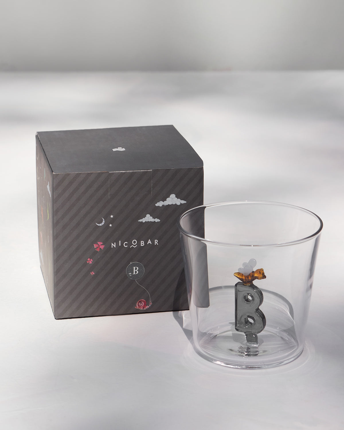 Clear Alphabet glass with a 3D letter B beside a charcoal Nicobar gift box.
