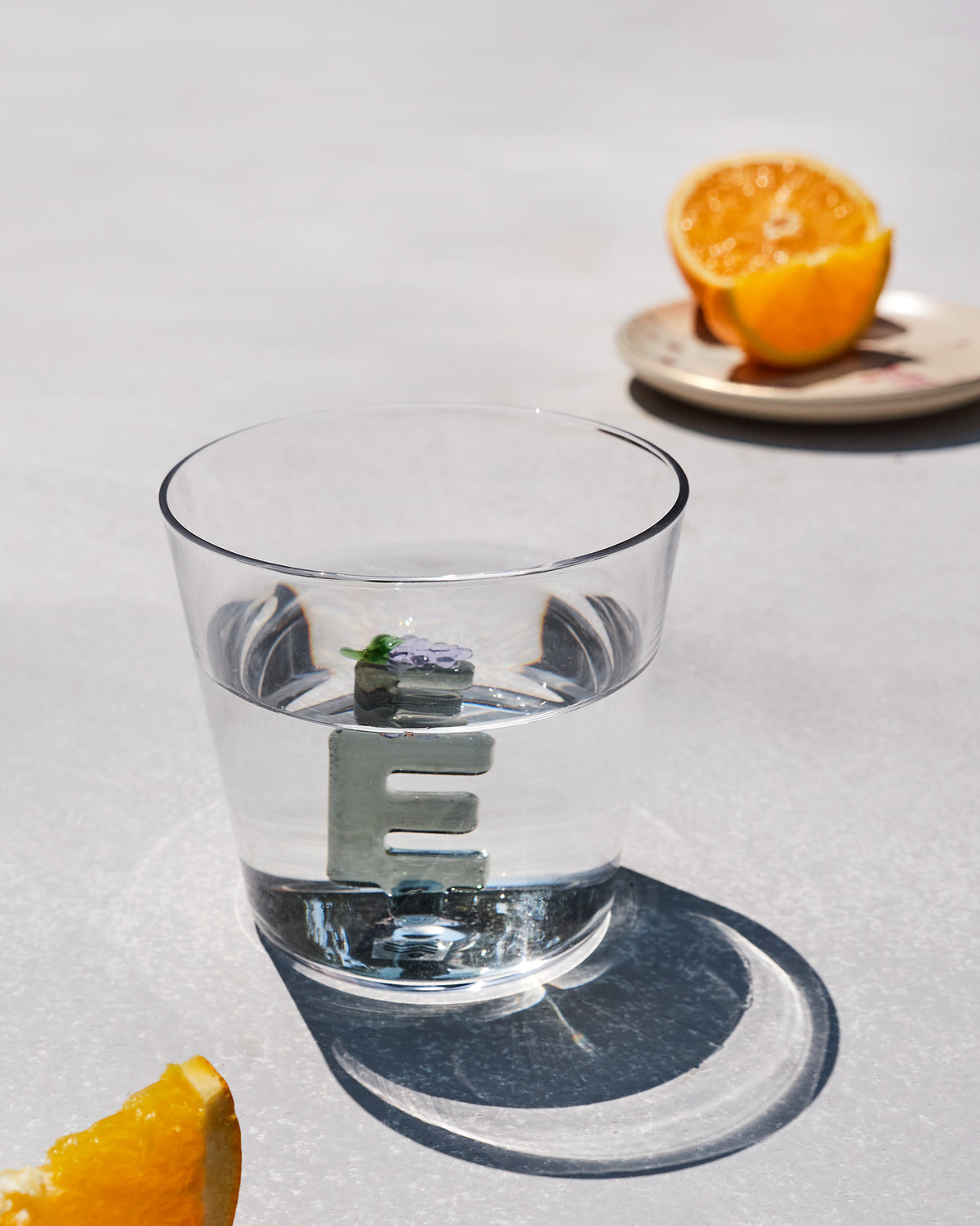 Clear Alphabet glass with a 3D letter E and purple flowers, filled with water.