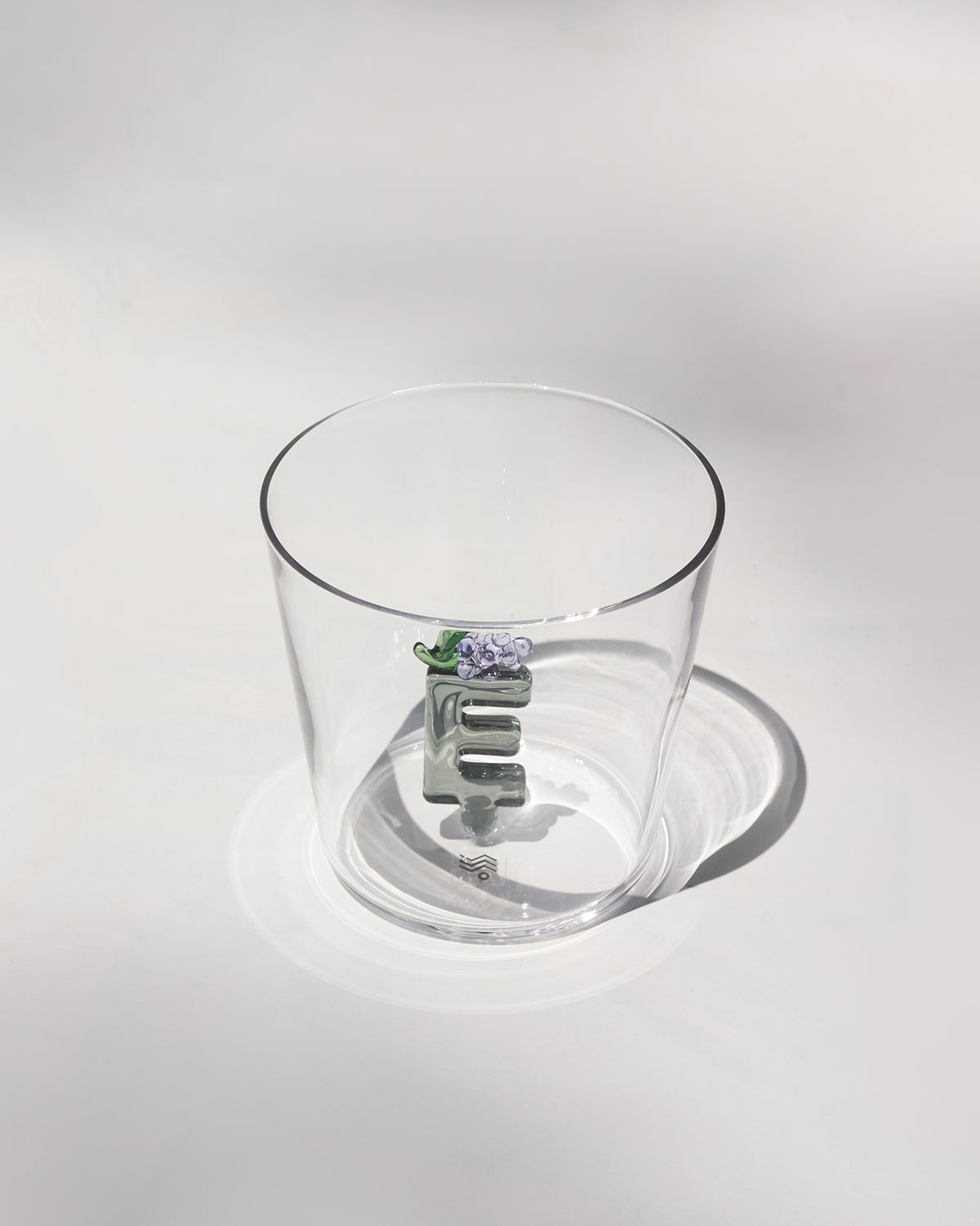 Clear tumbler with a 3D letter E topped by purple flowers and a green leaf.