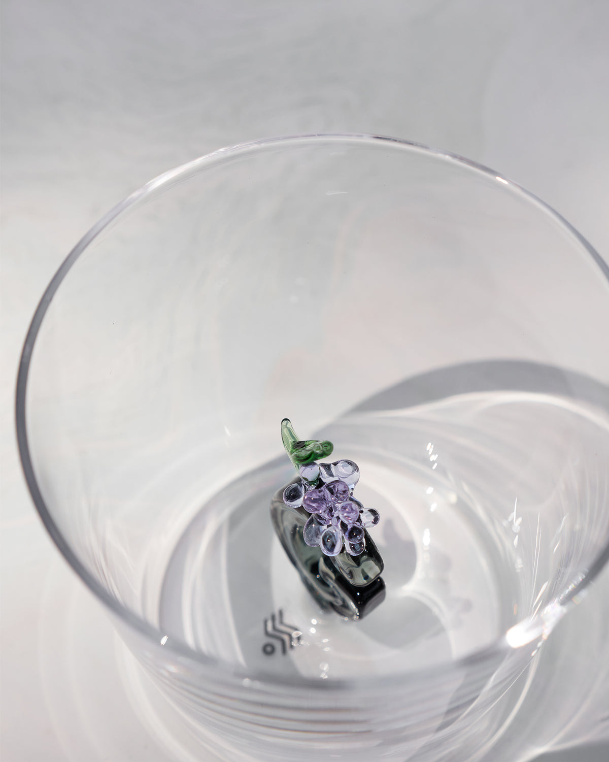 Looking down into a clear glass with purple flowers and a green leaf at the base.