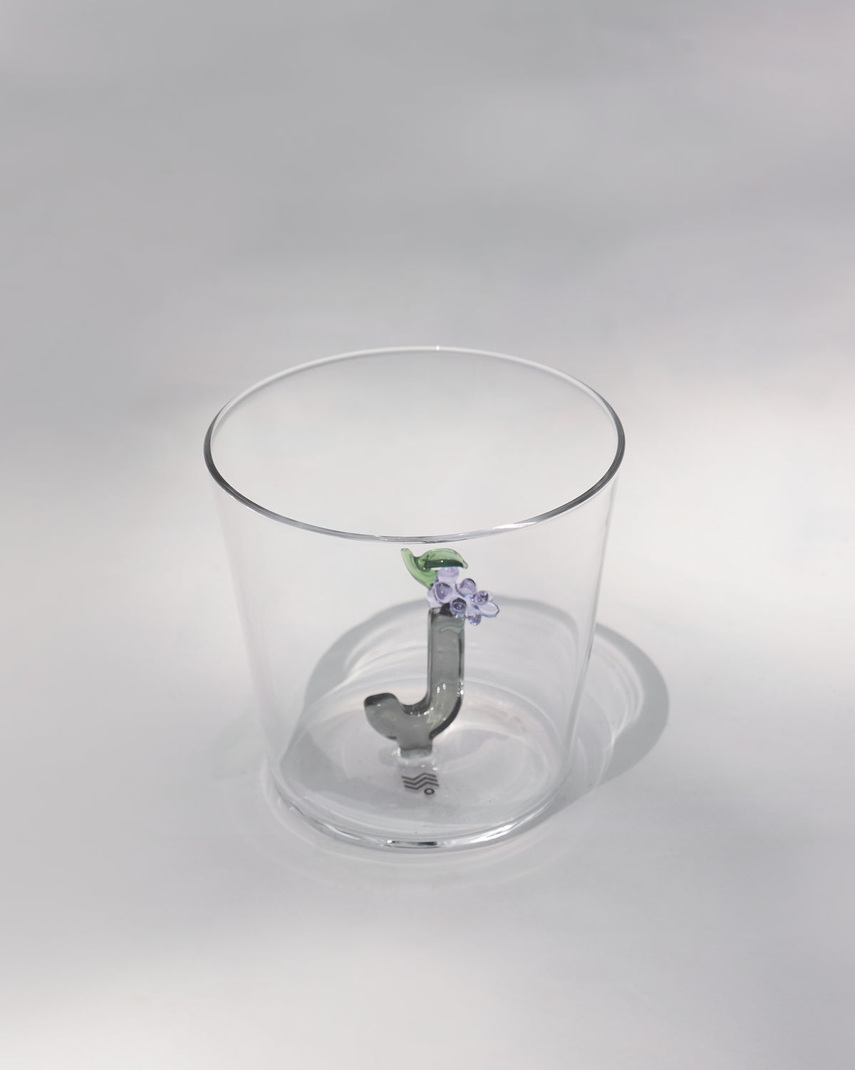 Clear tumbler with a 3D letter J topped by purple flowers and a green leaf.