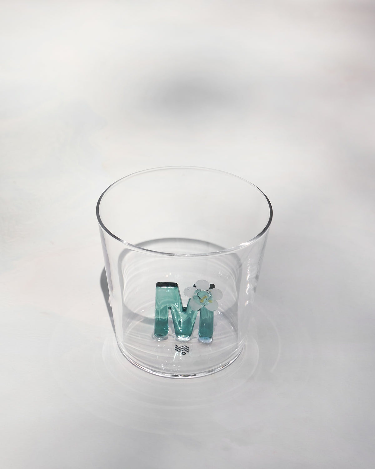 Clear Alphabet glass showing a teal letter M with a white flower at the base.