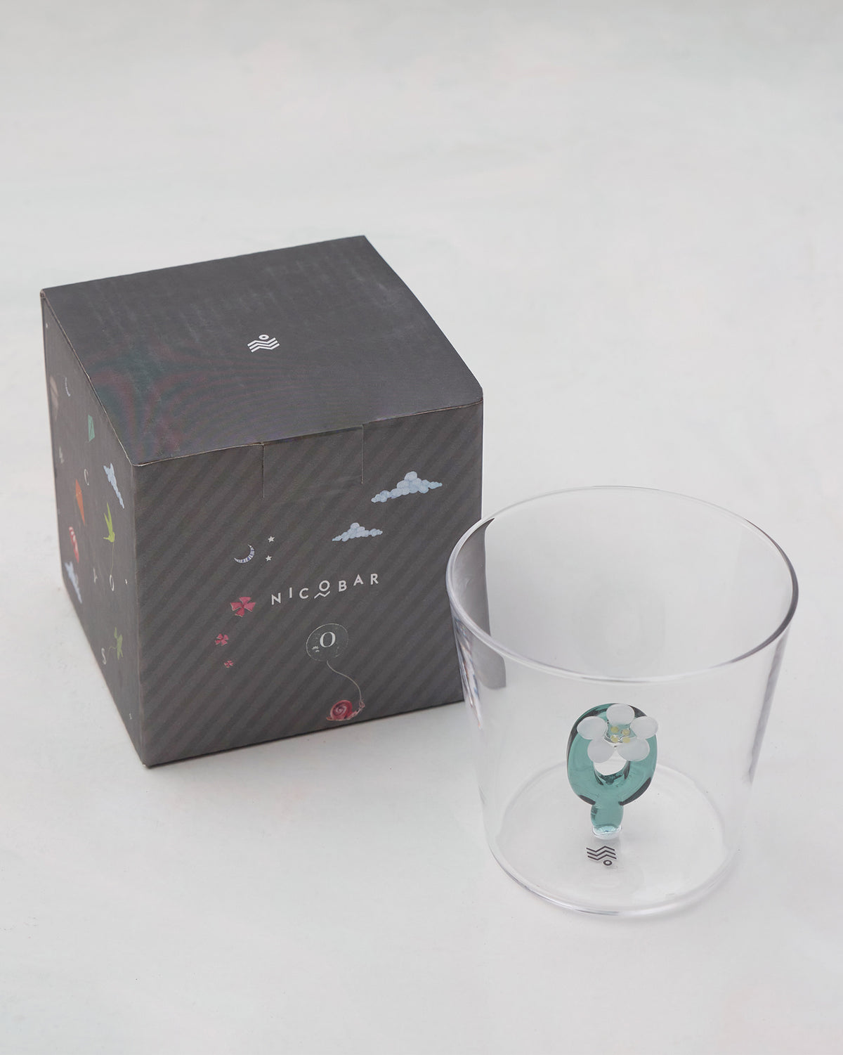 Alphabet glass with a teal letter O beside its charcoal Nicobar gift box.