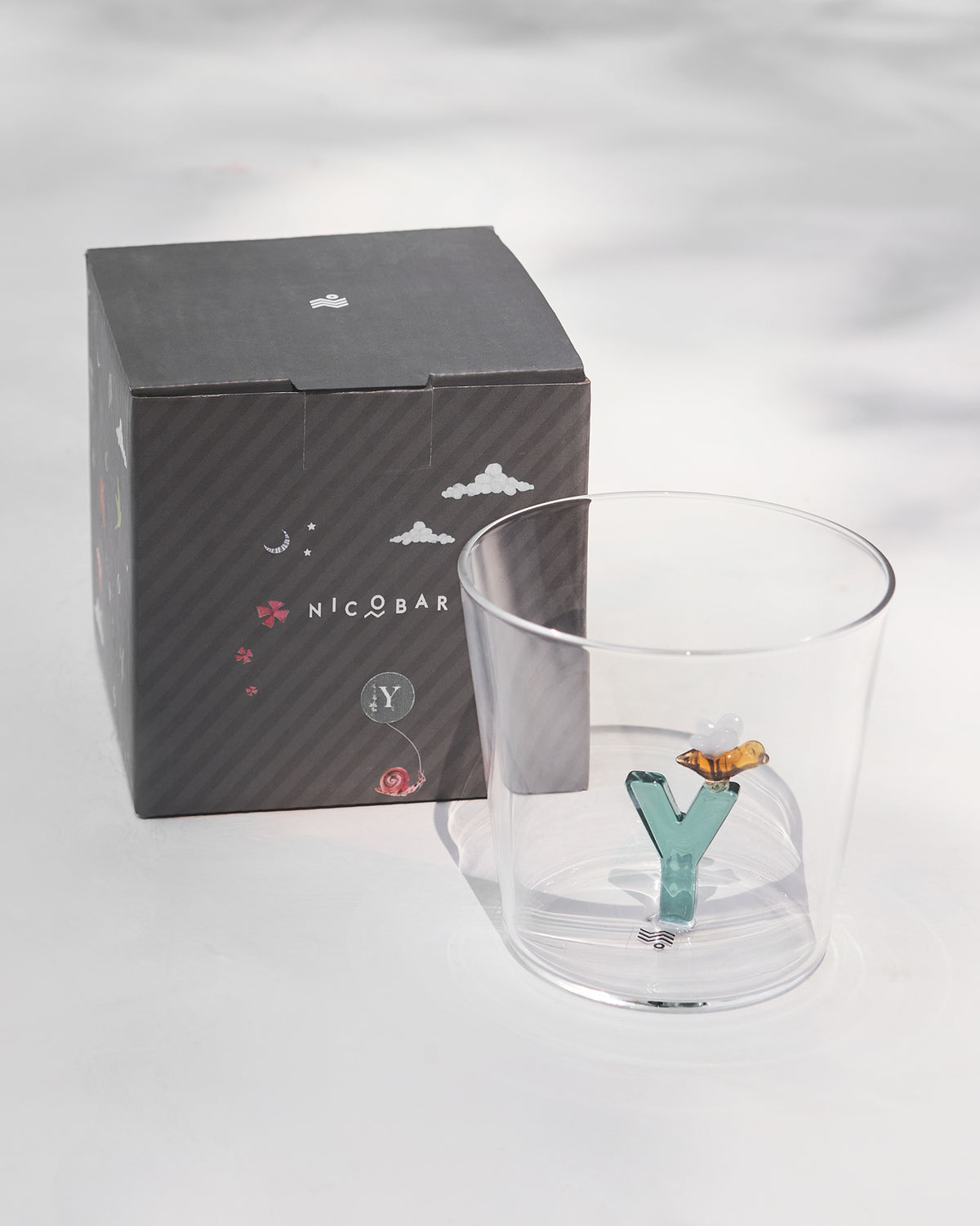 Alphabet glass with a teal letter Y beside its charcoal Nicobar gift box.