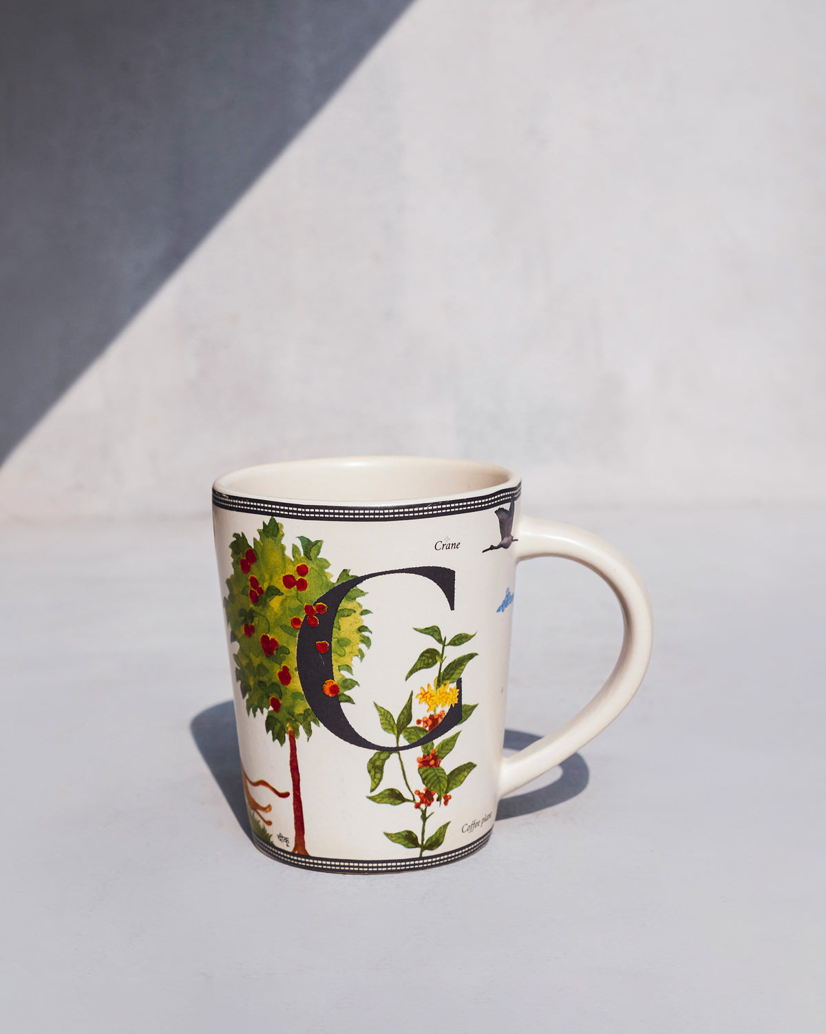 Chameli mug with letter C, coffee plant, and crane illustrations.