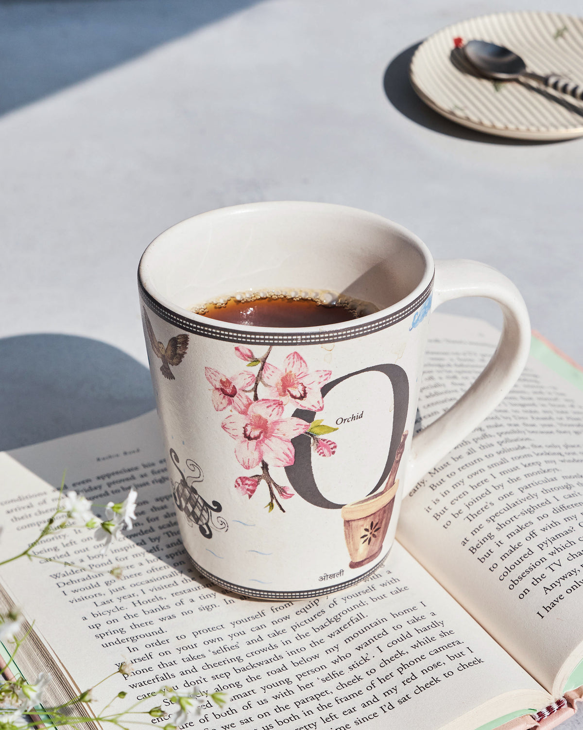 Cream Owl mug with orchid and letter O print, filled with coffee on a book.
