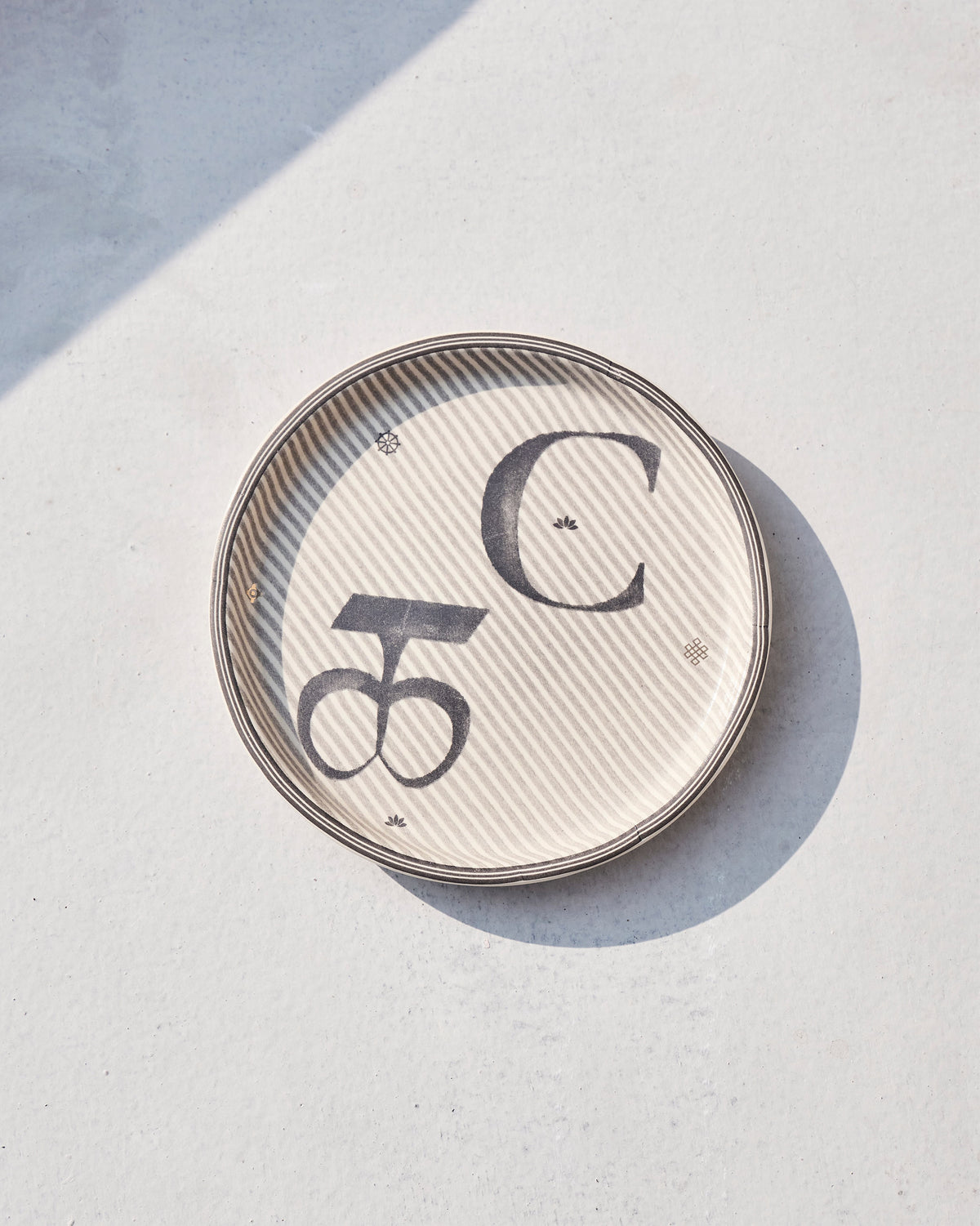 Akshar Coaster - C lying flat, showing the grey C glyph and beaded rim.