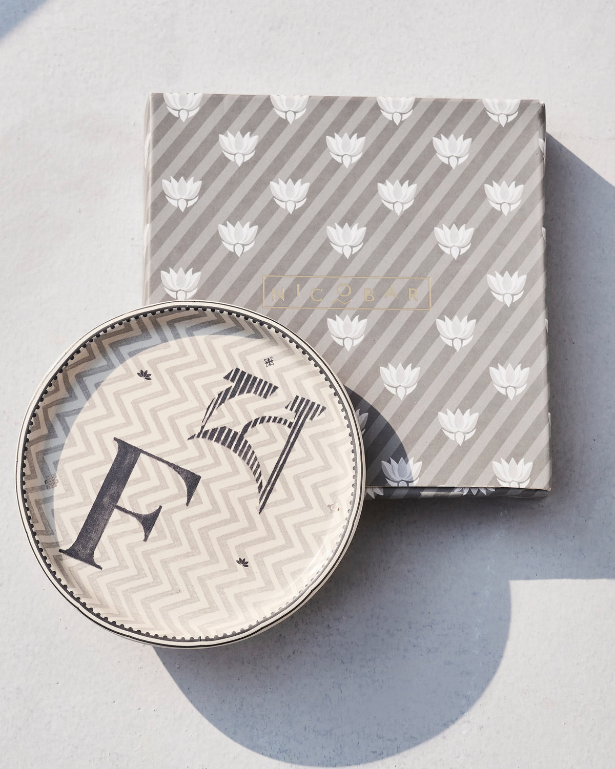 Akshar Coaster - F resting on its grey lotus-print box.
