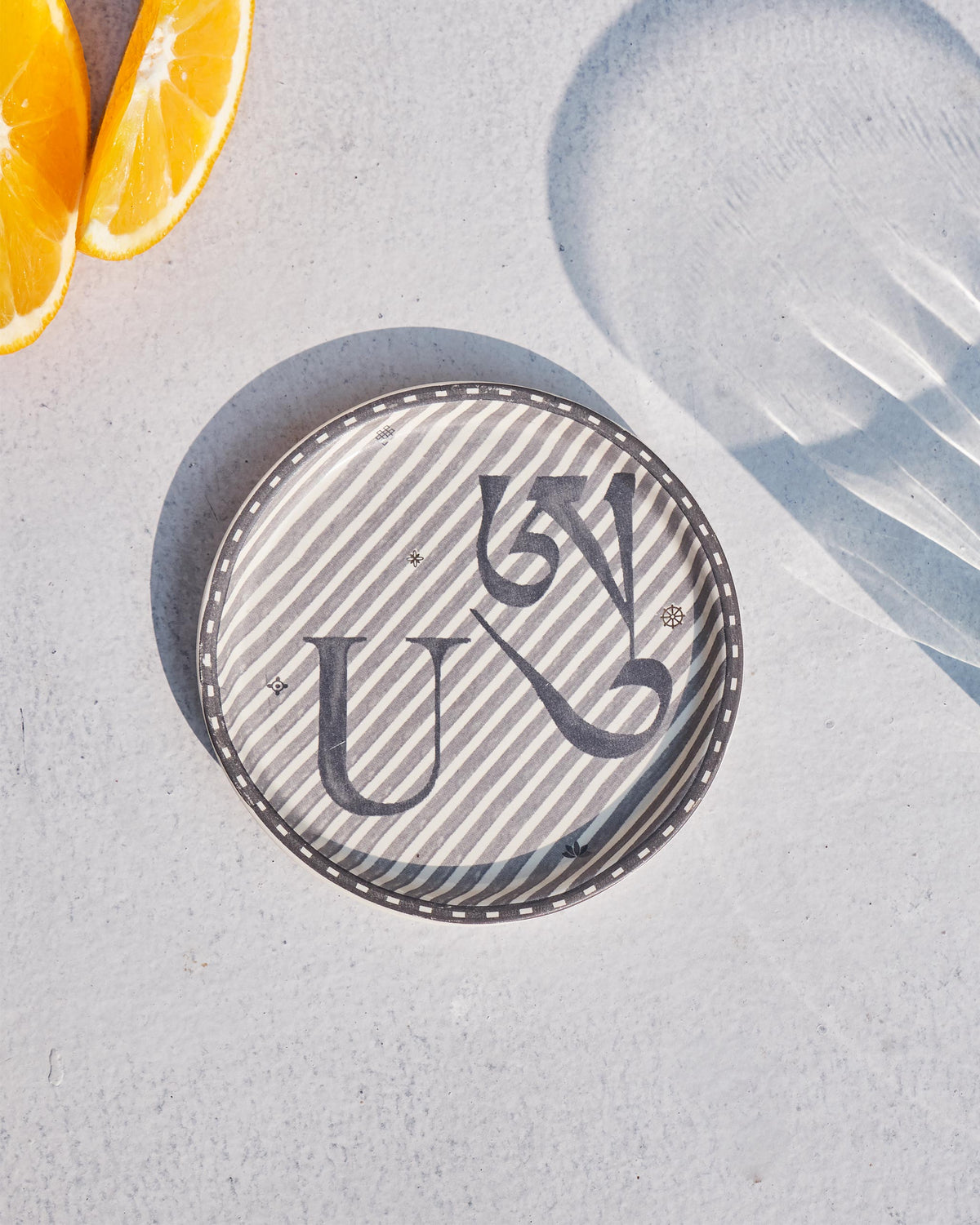 Akshar Coaster - U laid flat, showing the grey U glyph on diagonal stripes.