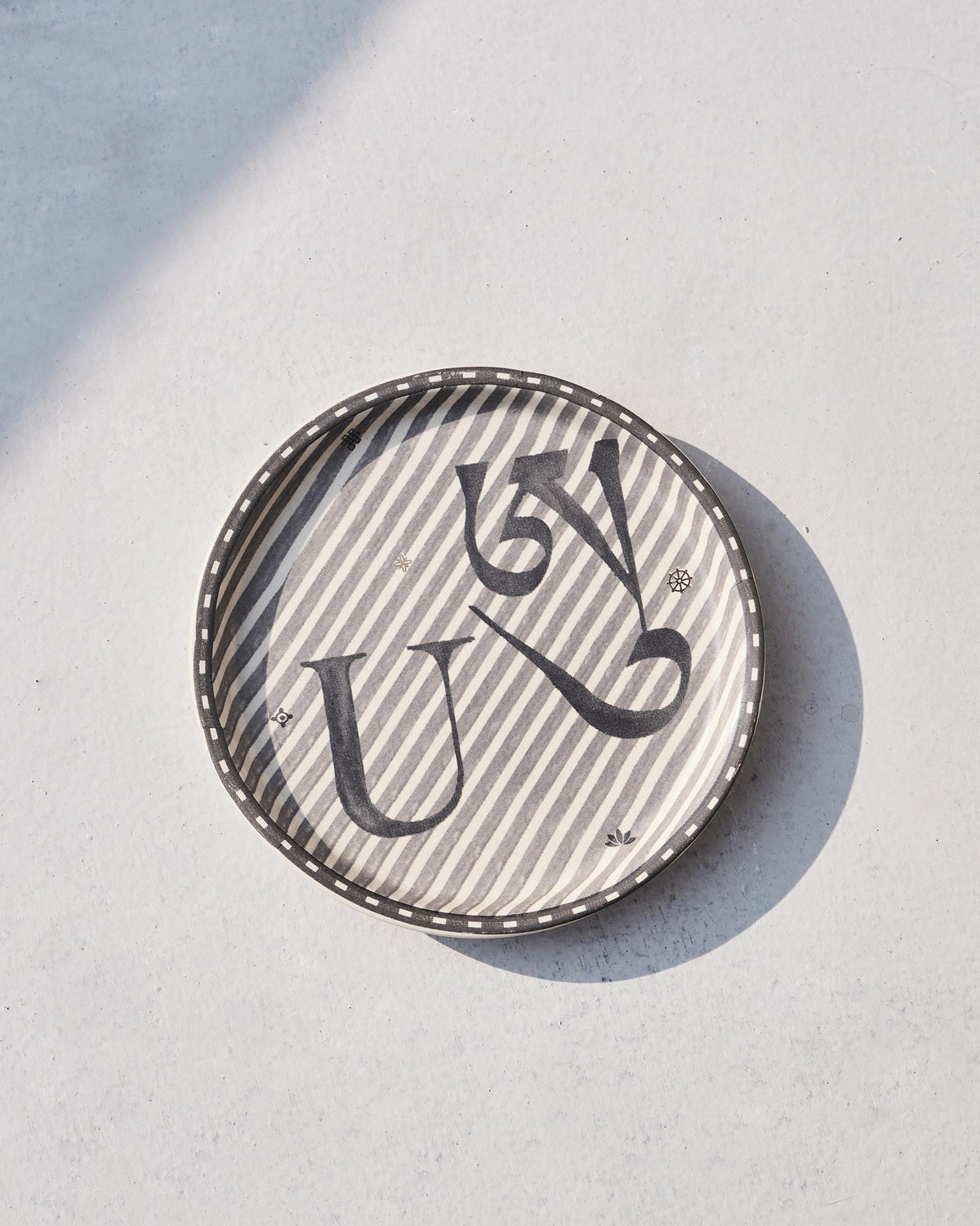 Akshar Coaster - U lying flat, showing its beaded rim and grey U glyph.