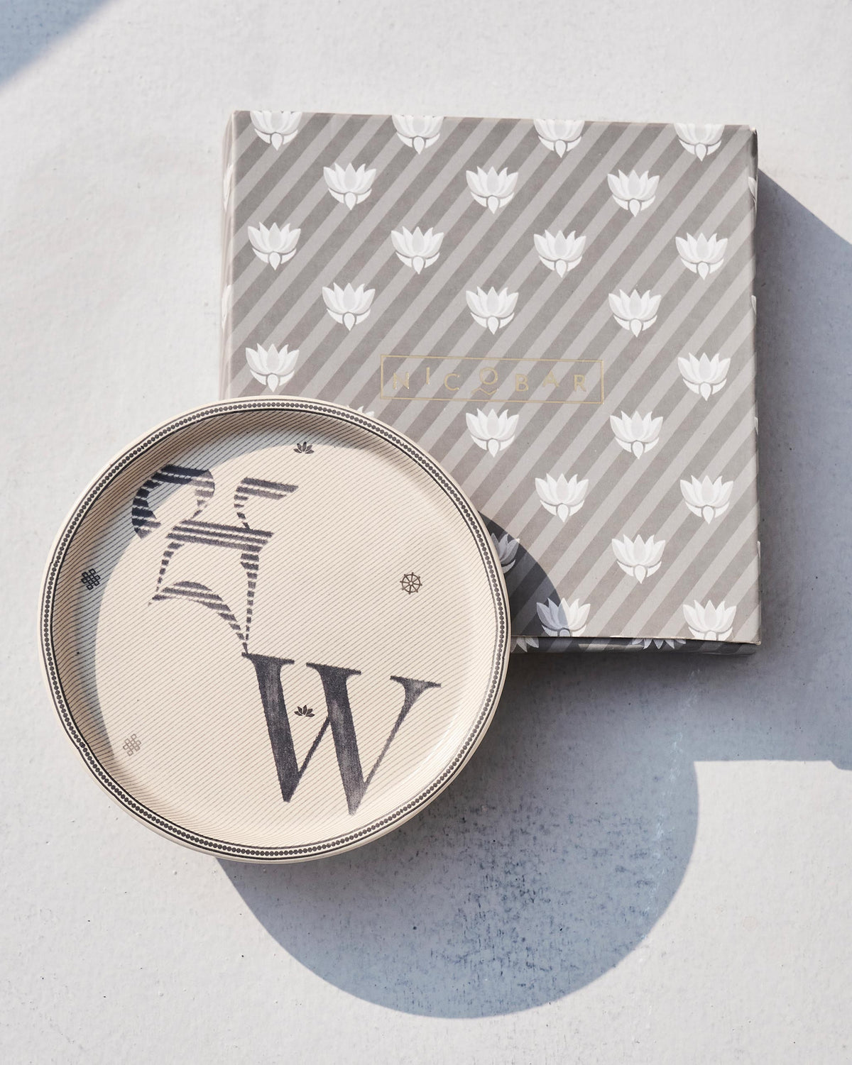 Akshar Coaster - W resting on its grey lotus-print box.