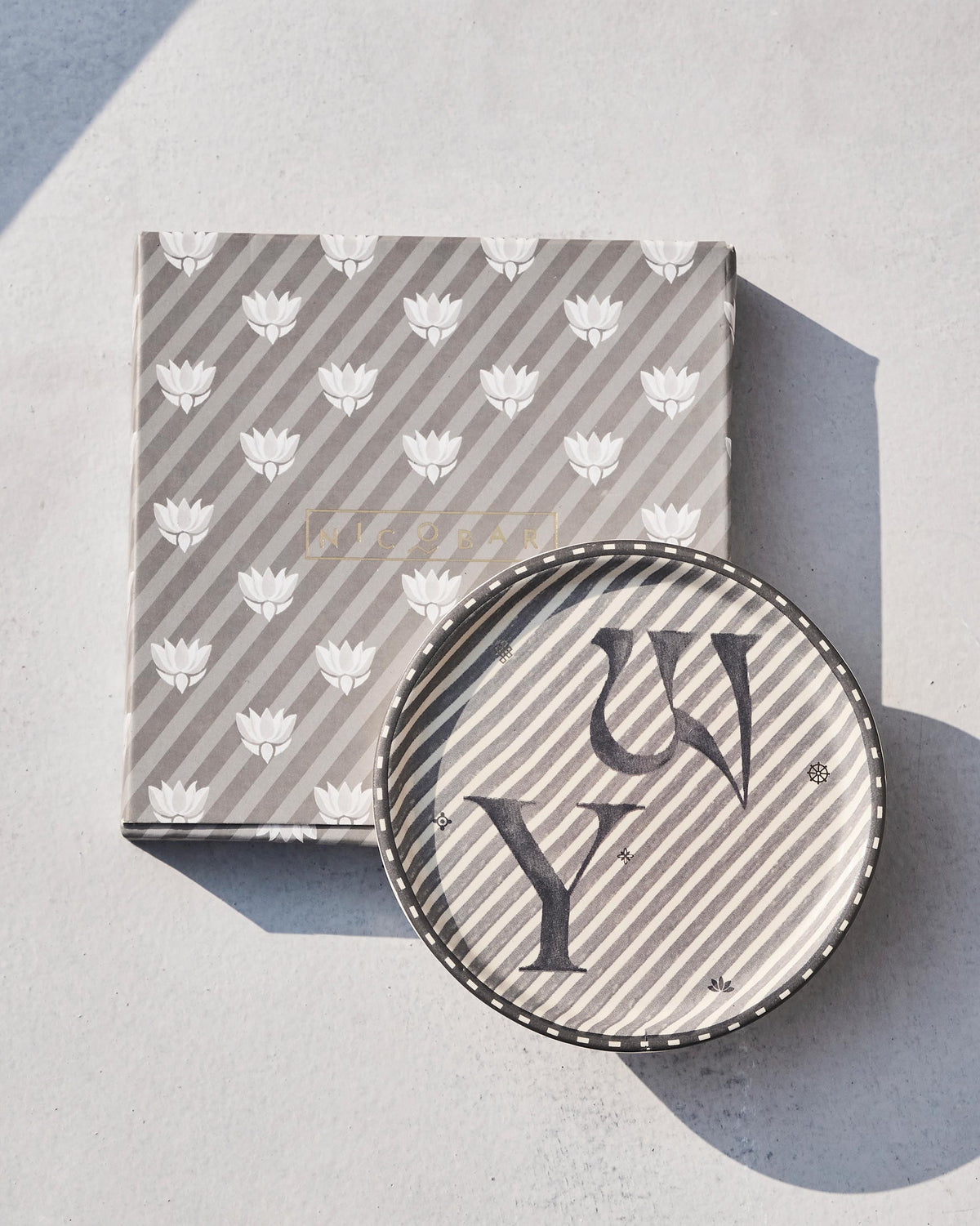 Akshar Coaster - Y resting on its grey lotus-print box.