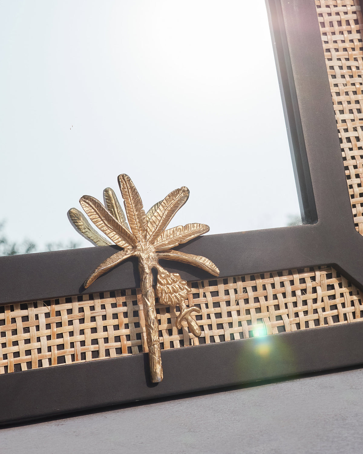 Close-up of the Pondicherry Mirror gold palm ornament on its black frame.