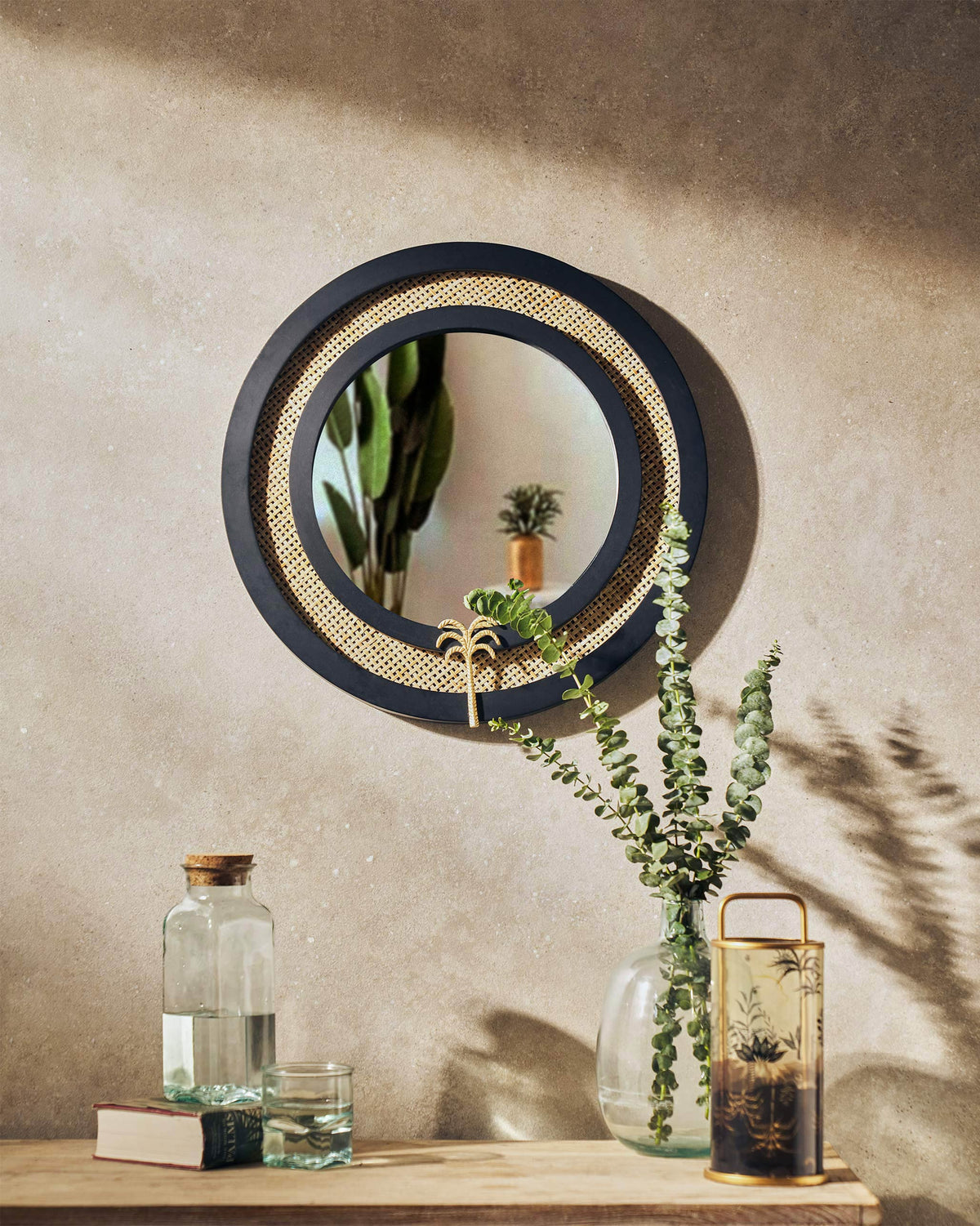 Suesgad Mirror with a black frame, woven cane ring and gold palm detail.