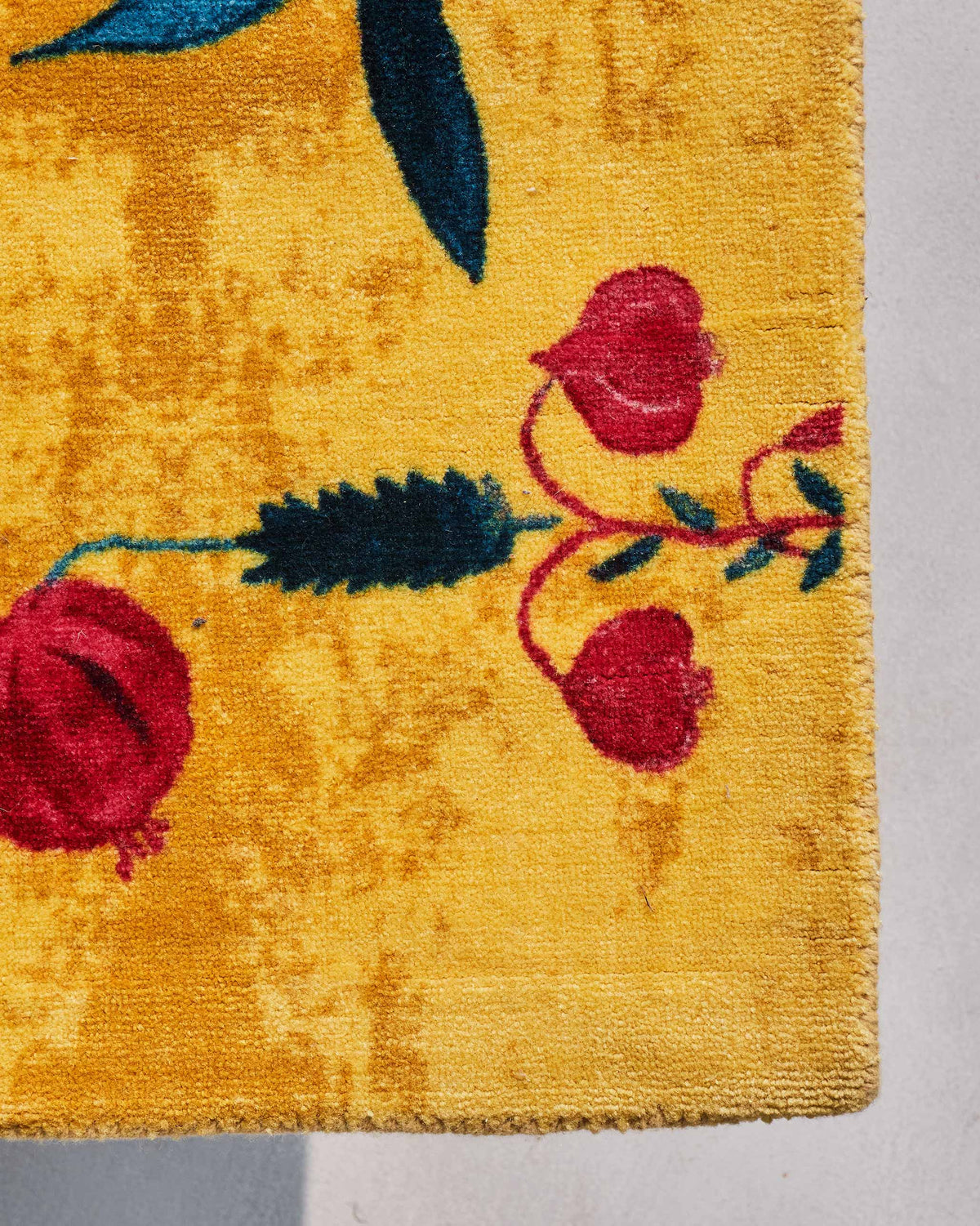 Corner of Woodland Rug in yellow with red buds and a teal leaf.
