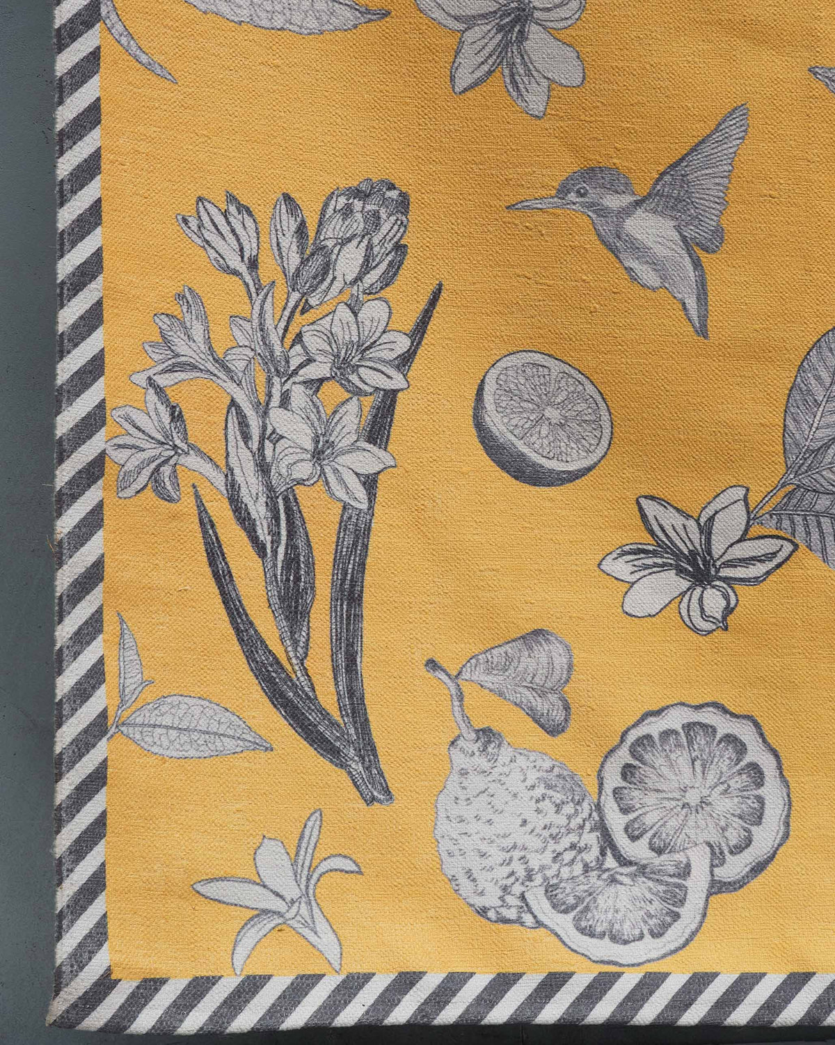 Close-up of Forest Rug in yellow corner with a hummingbird, flowers and lemon slice.