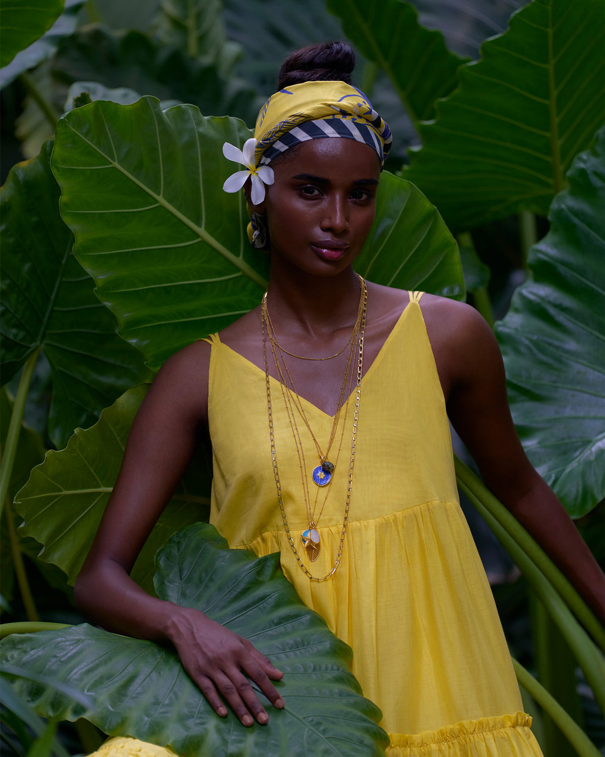 Person wearing a yellow V-neck tiered dress among tropical leaves.