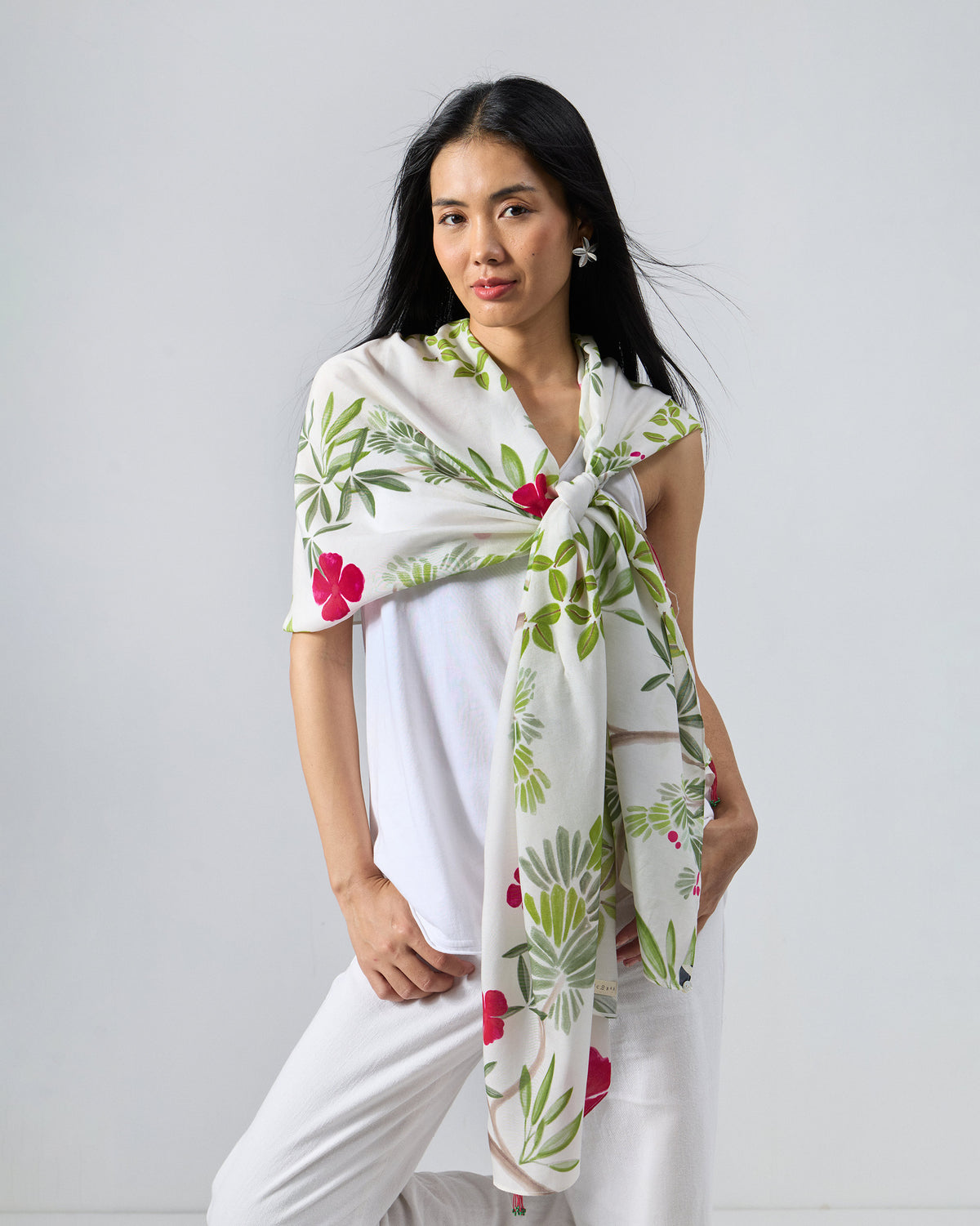 Person wearing the Alaya scarf in white with green foliage and red flowers.