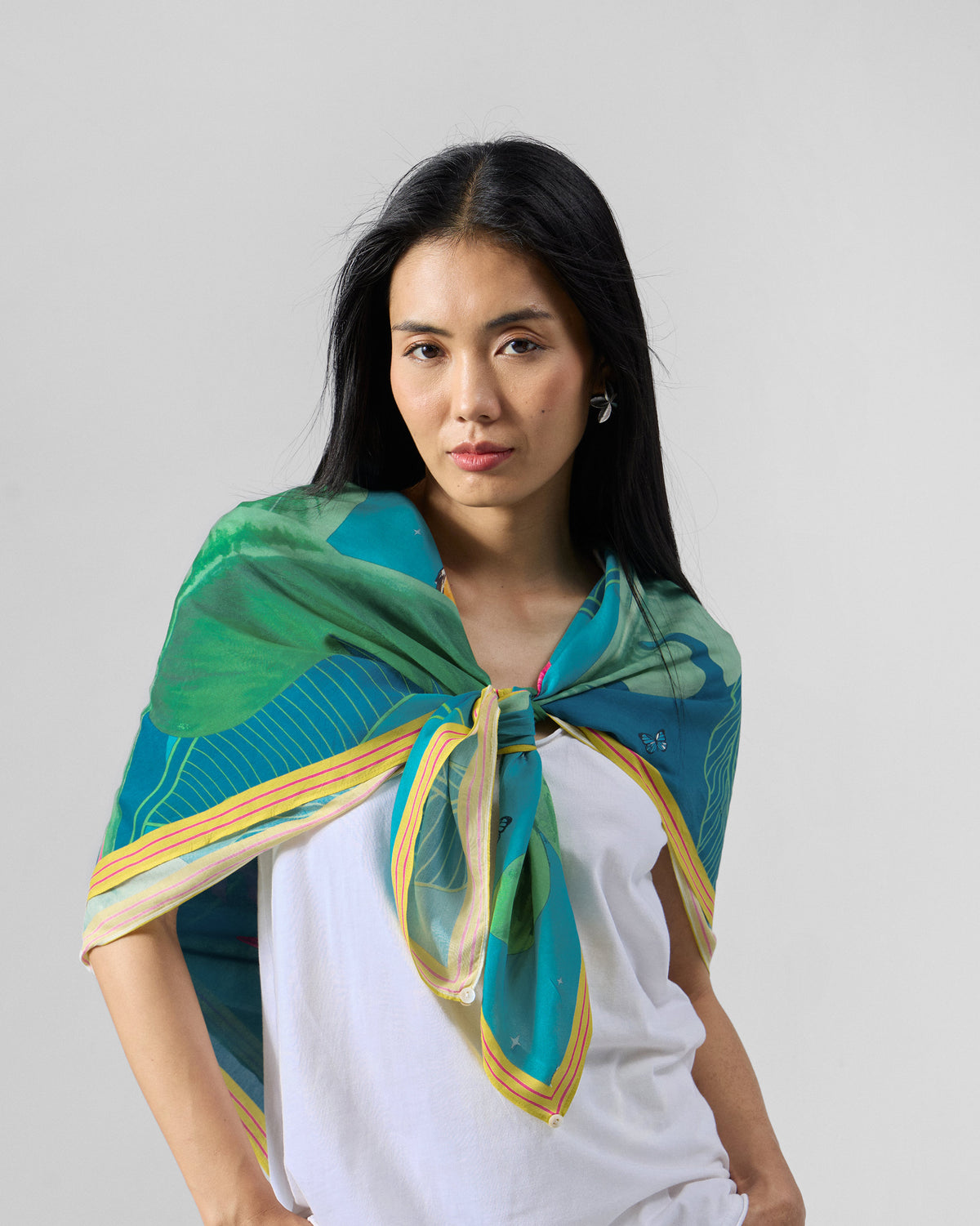Person wearing a green Hideaway scarf with a teal leaf print and striped edge.