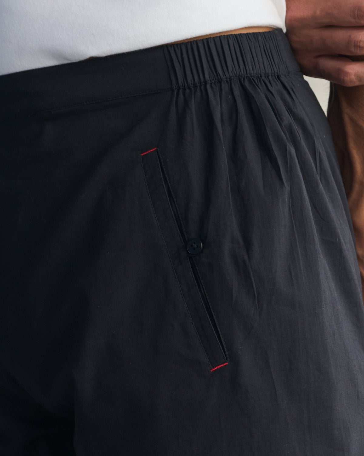 Close-up of black Kurta Pants showing the elasticated waistband and red-edged side pocket.