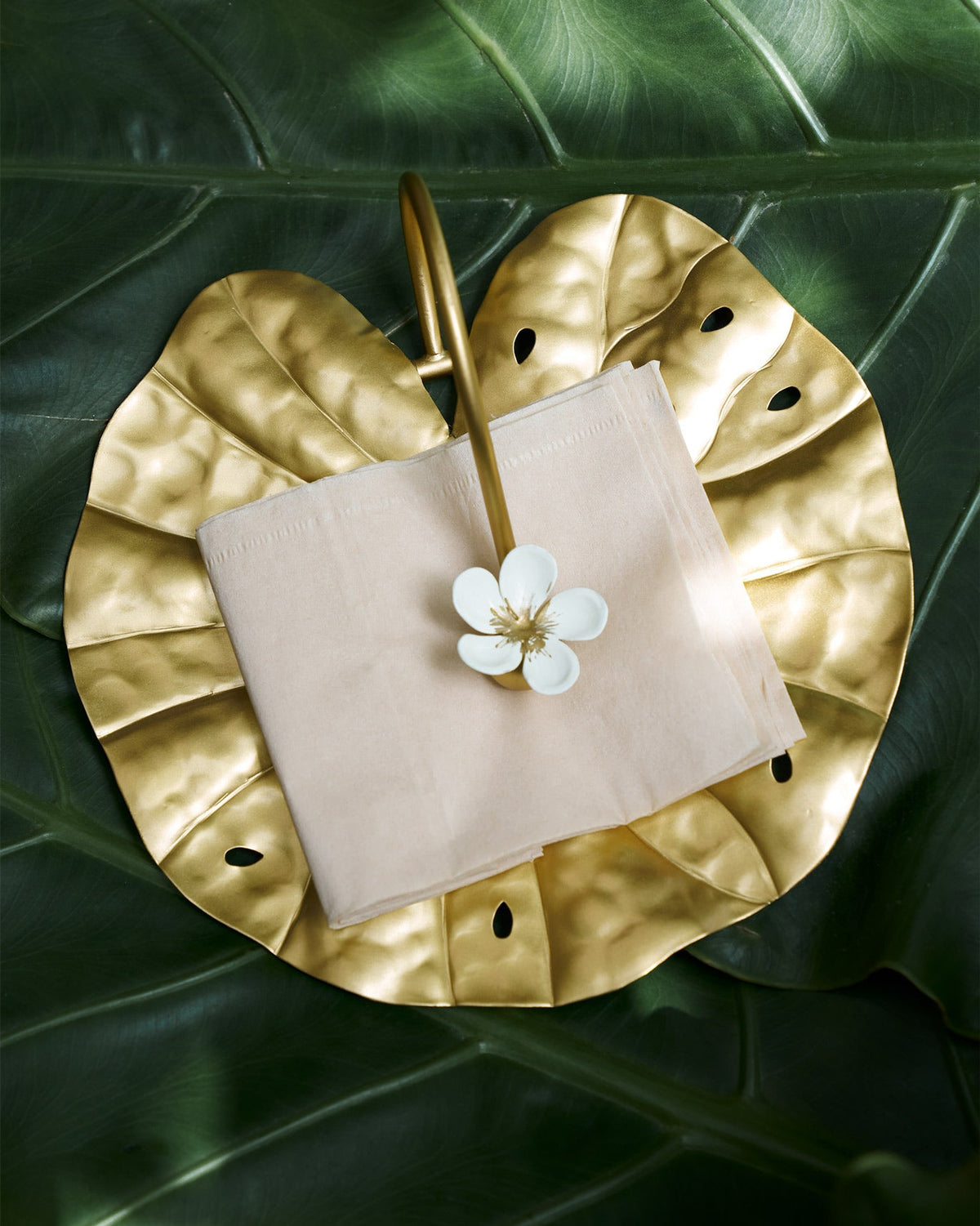 Gold Padma napkin holder shaped like a lotus leaf, holding ivory napkins.