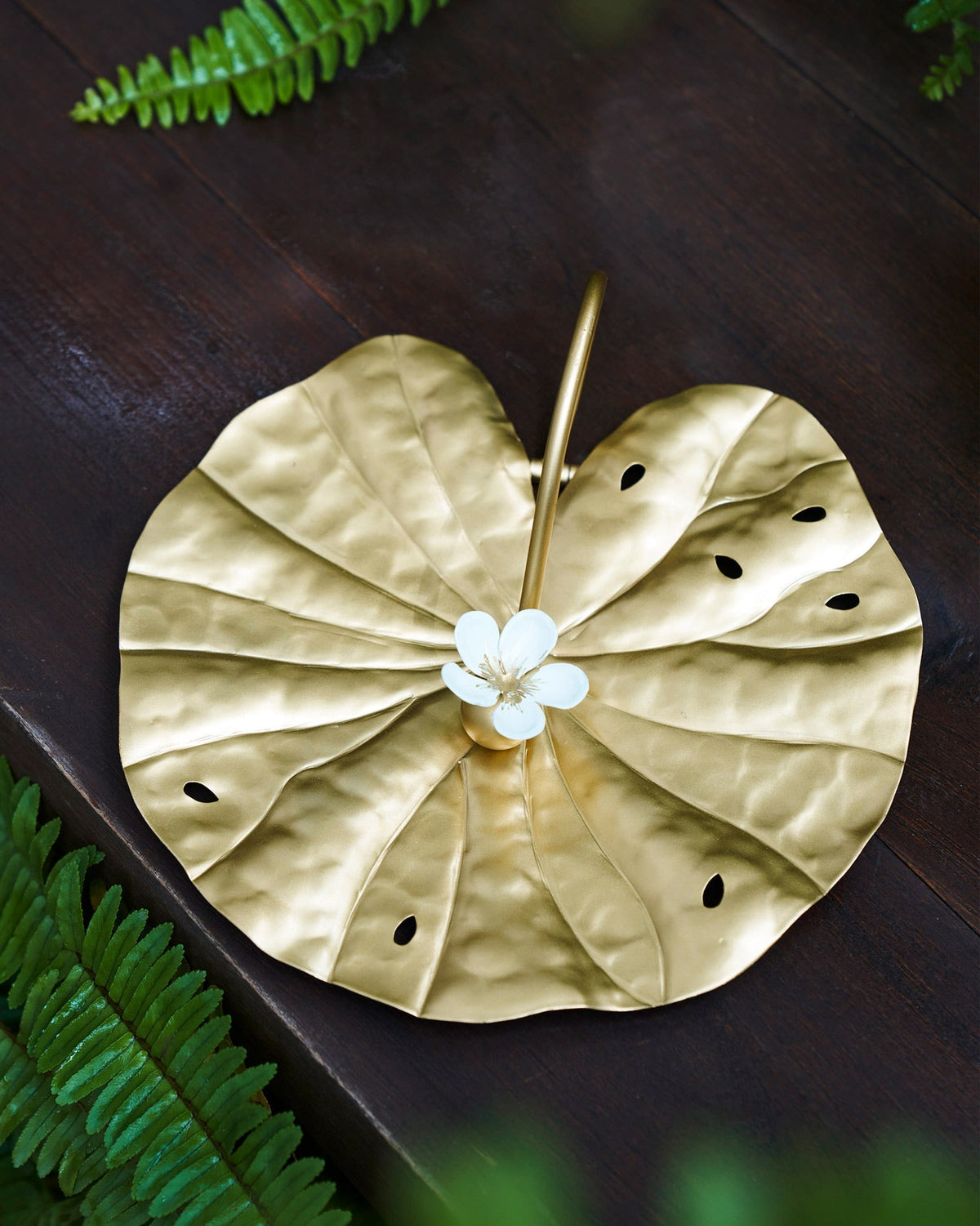 Gold Padma lotus-leaf napkin holder with a white flower on a wood table.