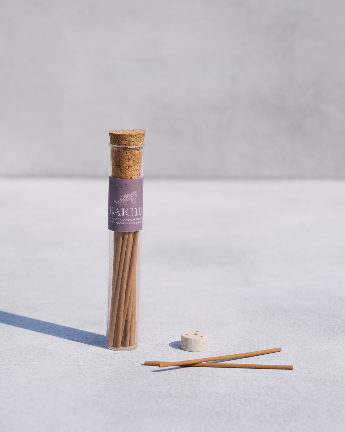 Bakhu incense sticks in a tube beside loose sticks and a white holder.