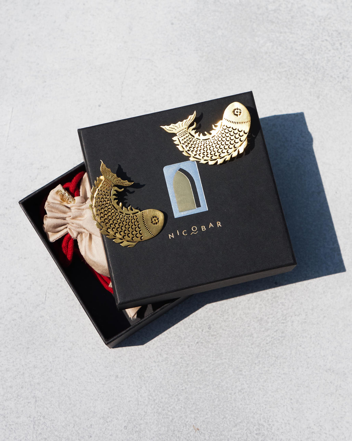 Pair of gold Meen Earrings resting on a Nicobar gift box.