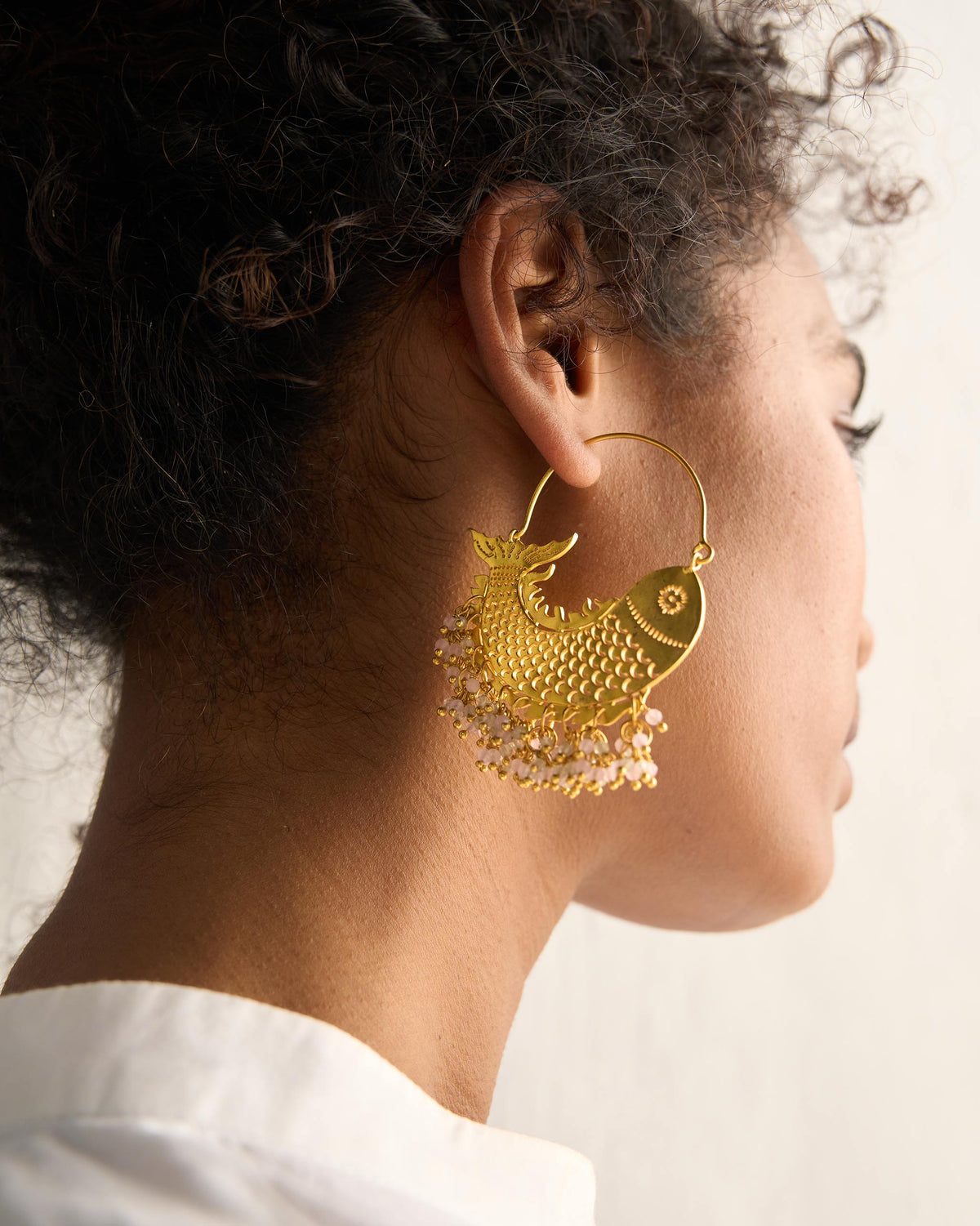 Person wearing a gold Meen Bali with a fish shape and beaded drops.