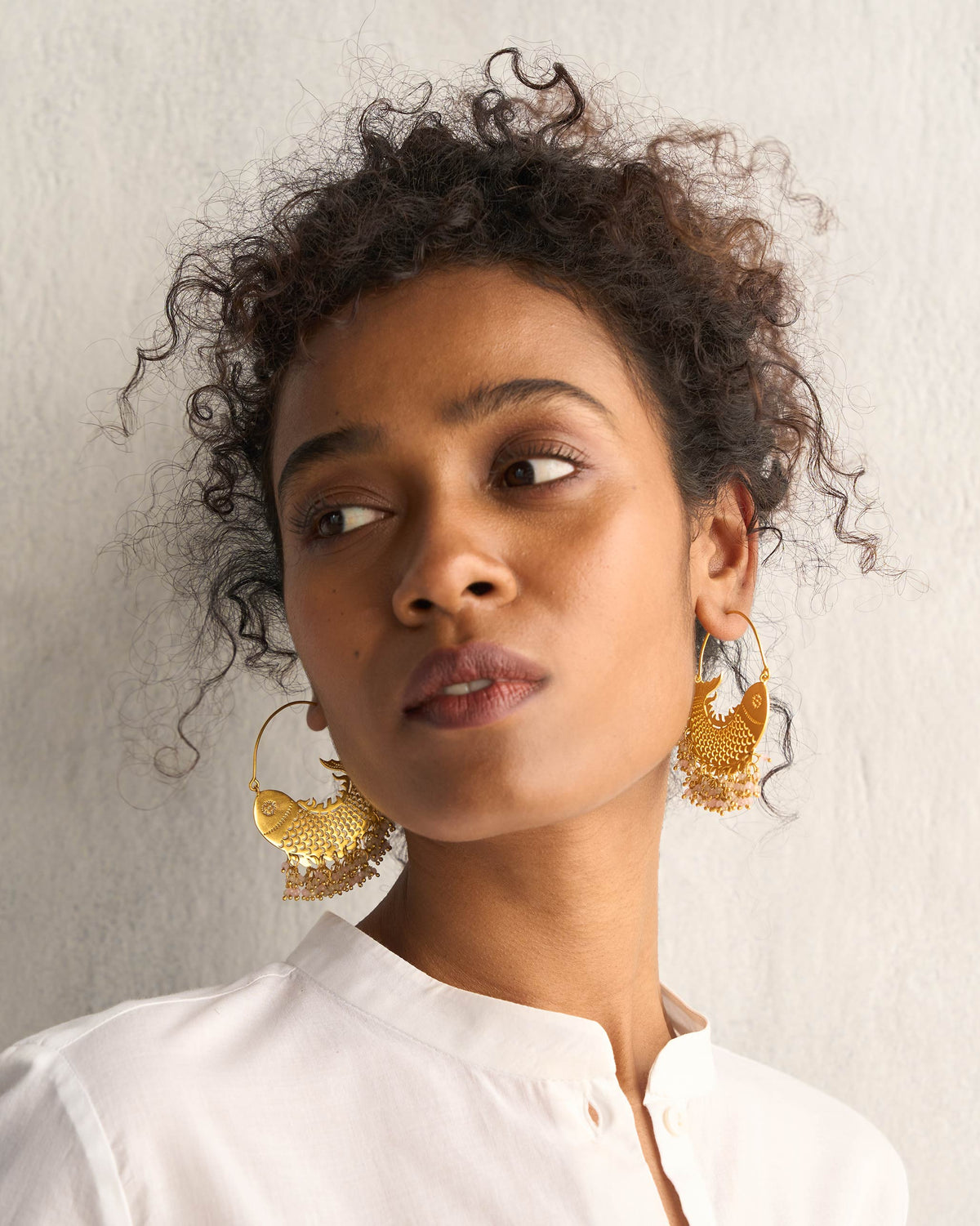 Person wearing gold Meen Bali earrings with beaded drops.