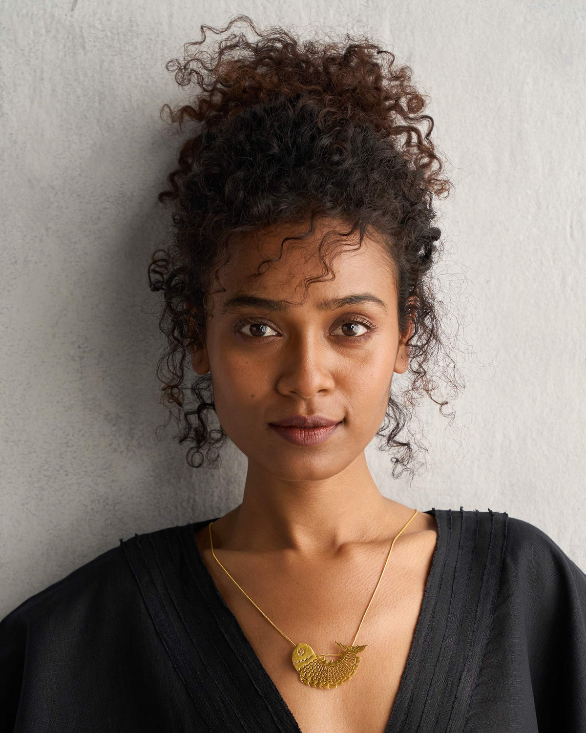 Person wearing a gold Meen Pendant on a fine chain.