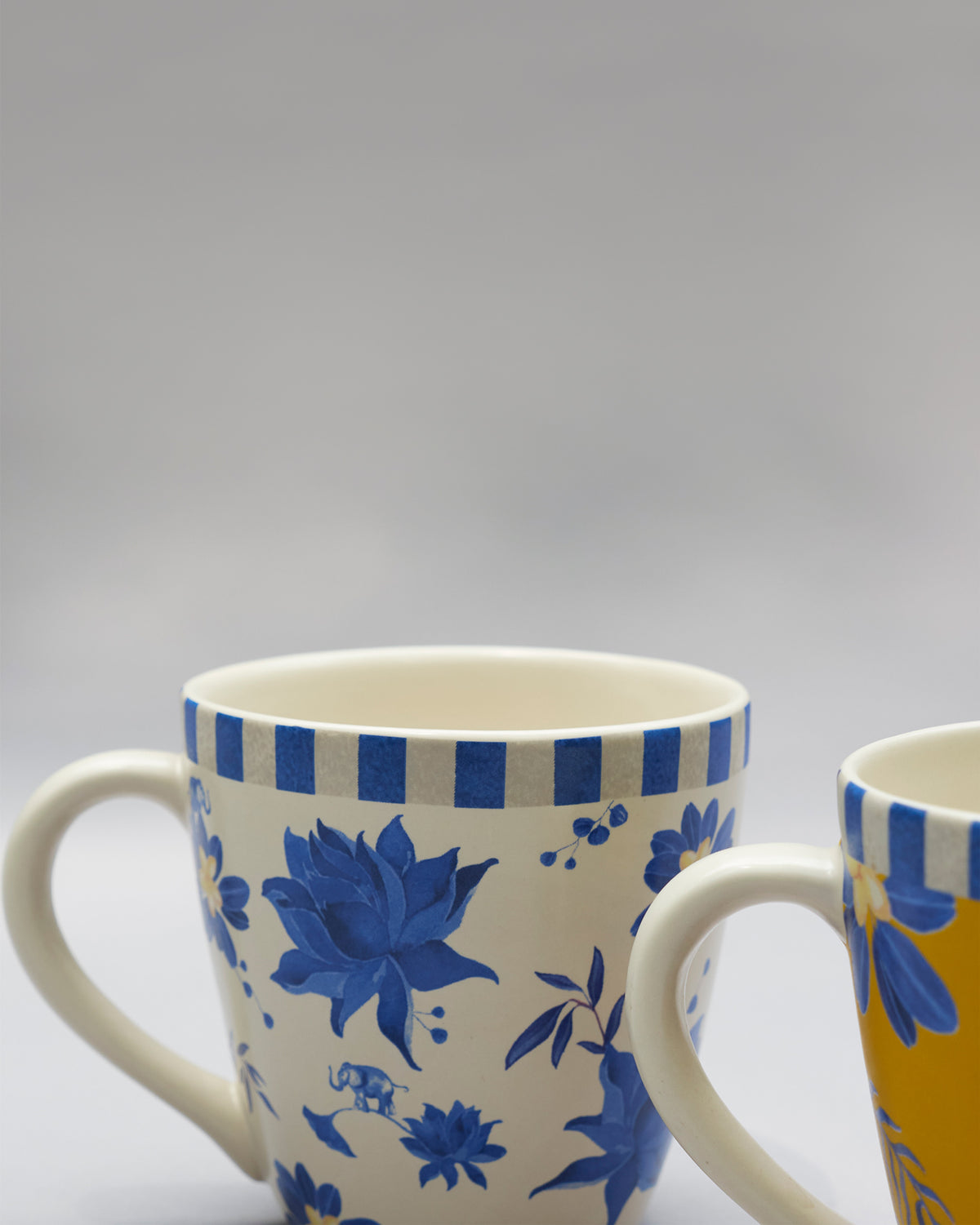 Close-up of a cream Panas mug with blue florals beside a yellow companion mug.