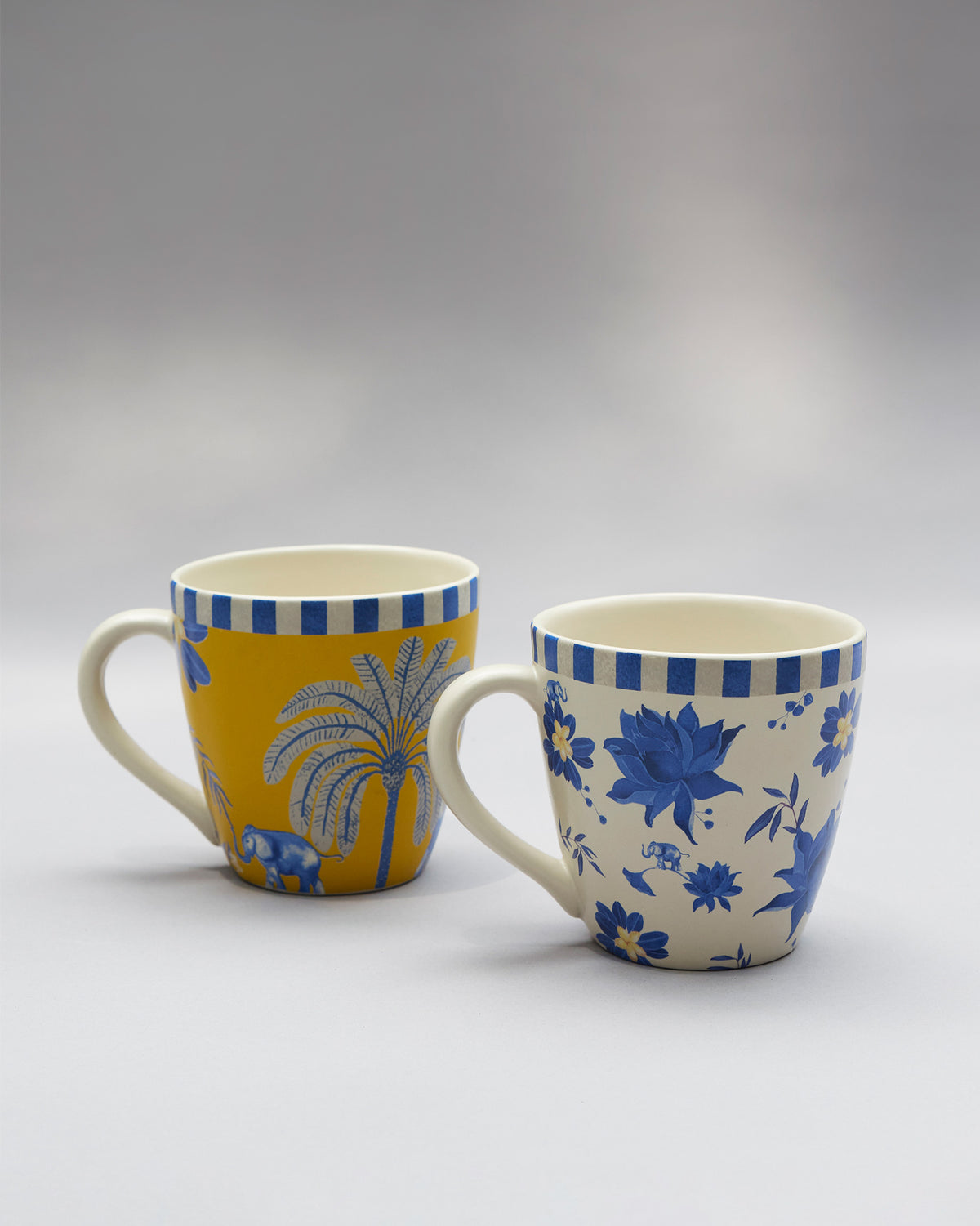 Yellow Panas mug with a palm and elephant beside a cream floral Panas mug.